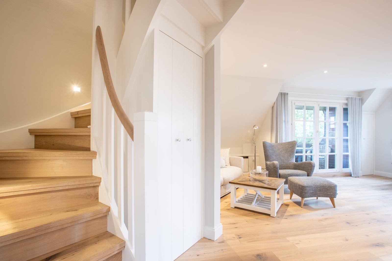 Helle Treppe führt in ein Wohnzimmer mit Sitzmöbeln und Fenster.