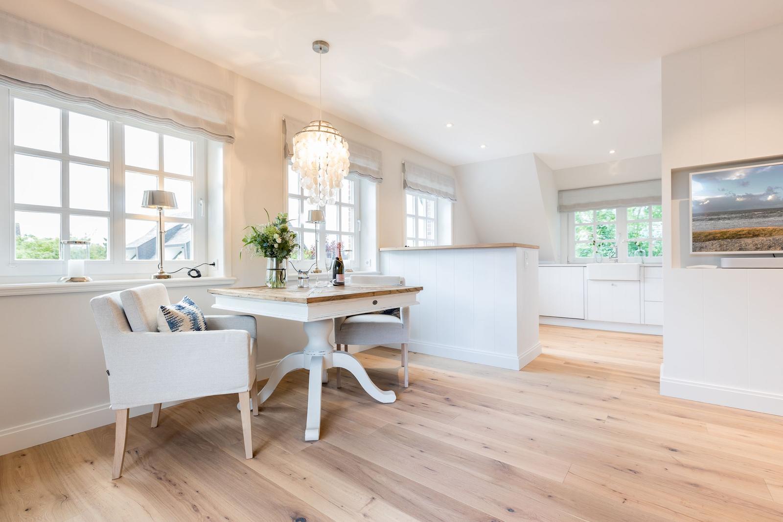 Essbereich mit Tisch, Stühlen und Fenstern. Küche mit Arbeitsplatte und TV.