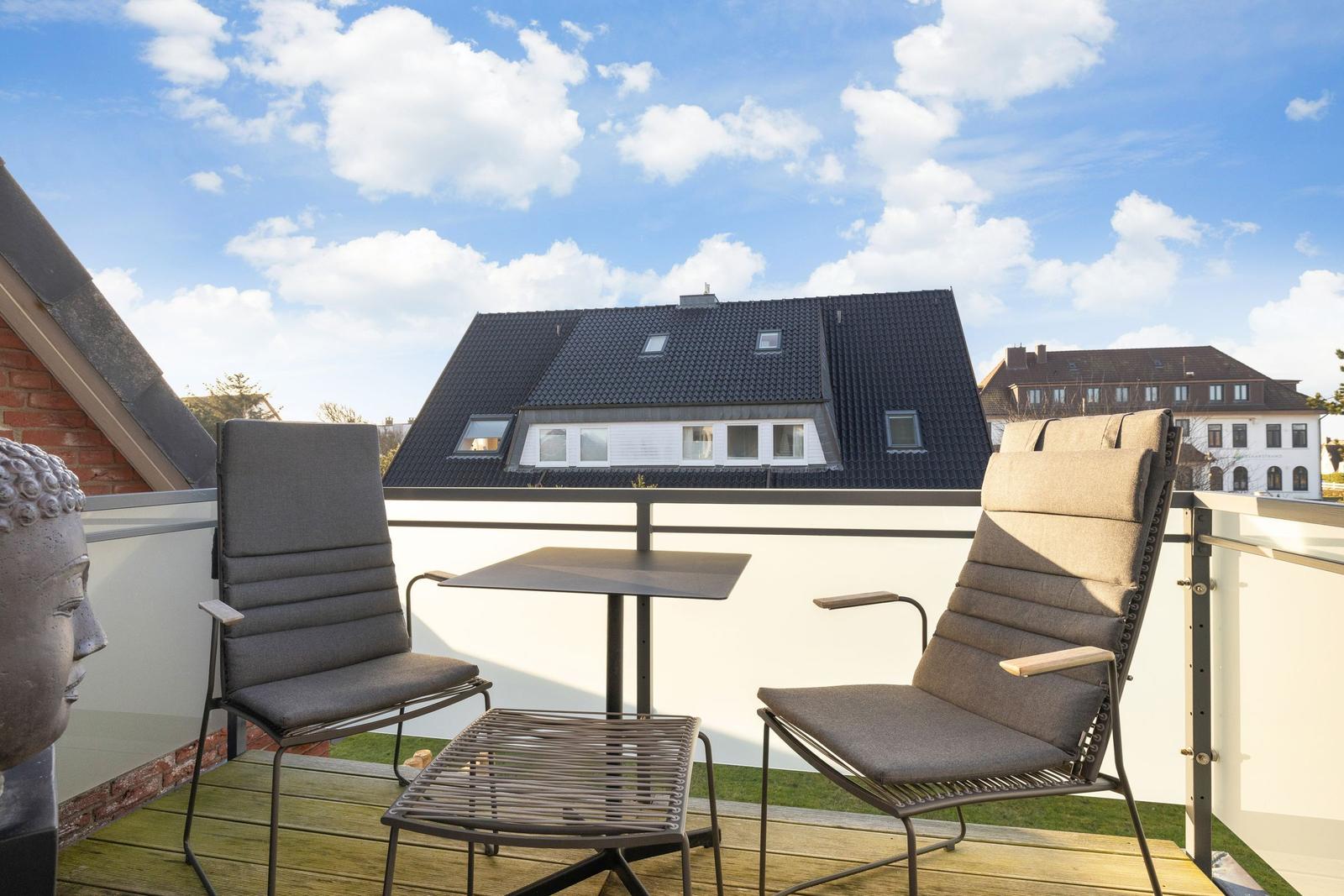 Terrace with two chairs, table, and Buddha statue. View of rooftops and sky.