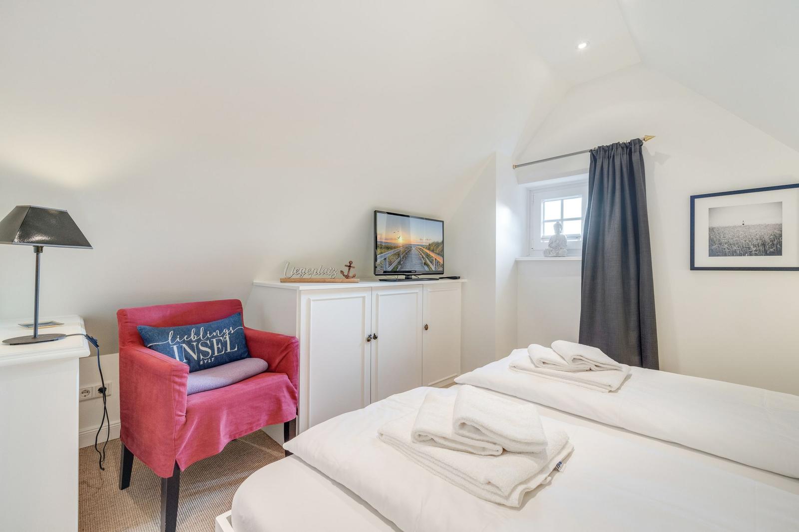 Bedroom with bed, TV, and red armchair.