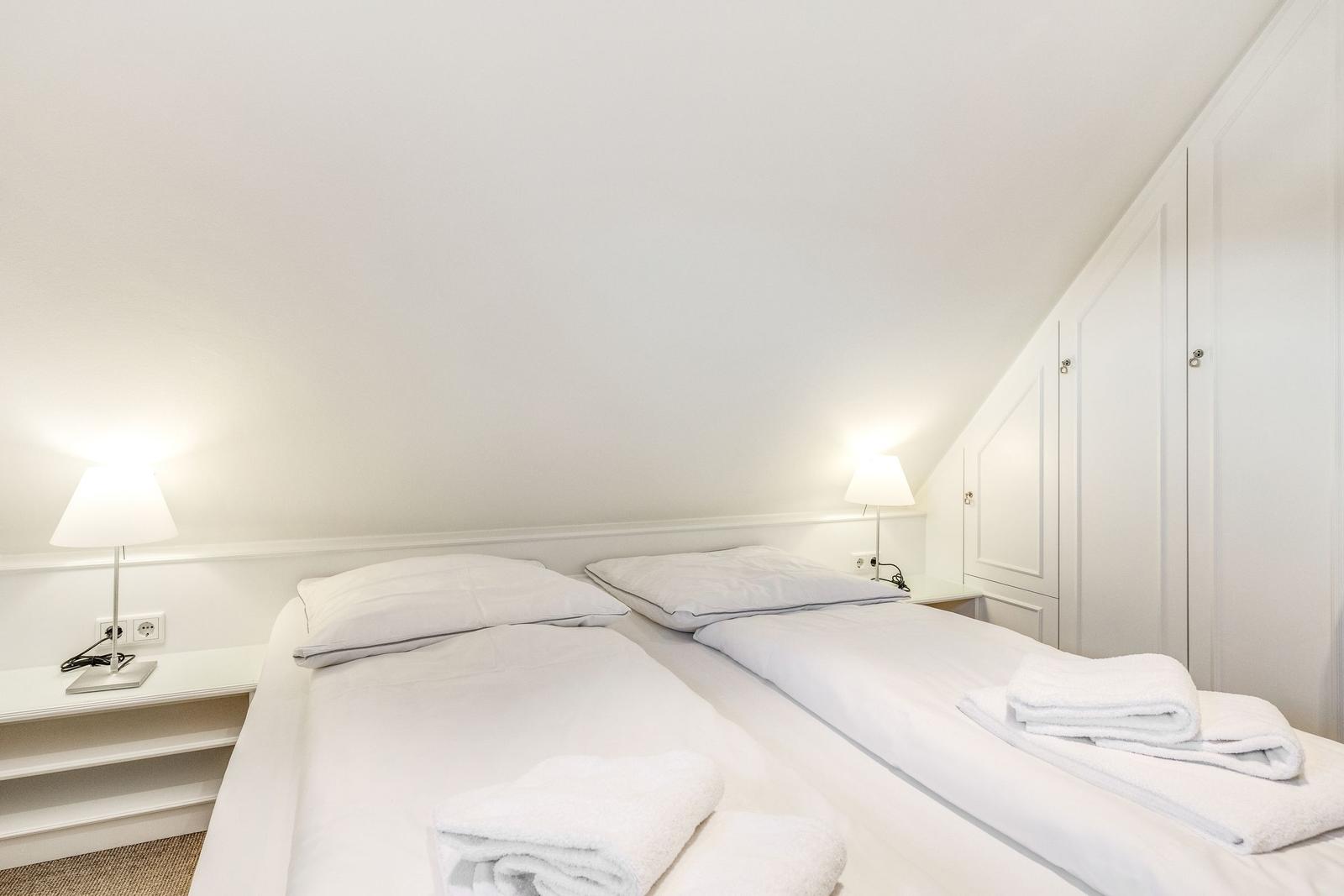 Room with two beds, white walls, and nightstands with lamps.