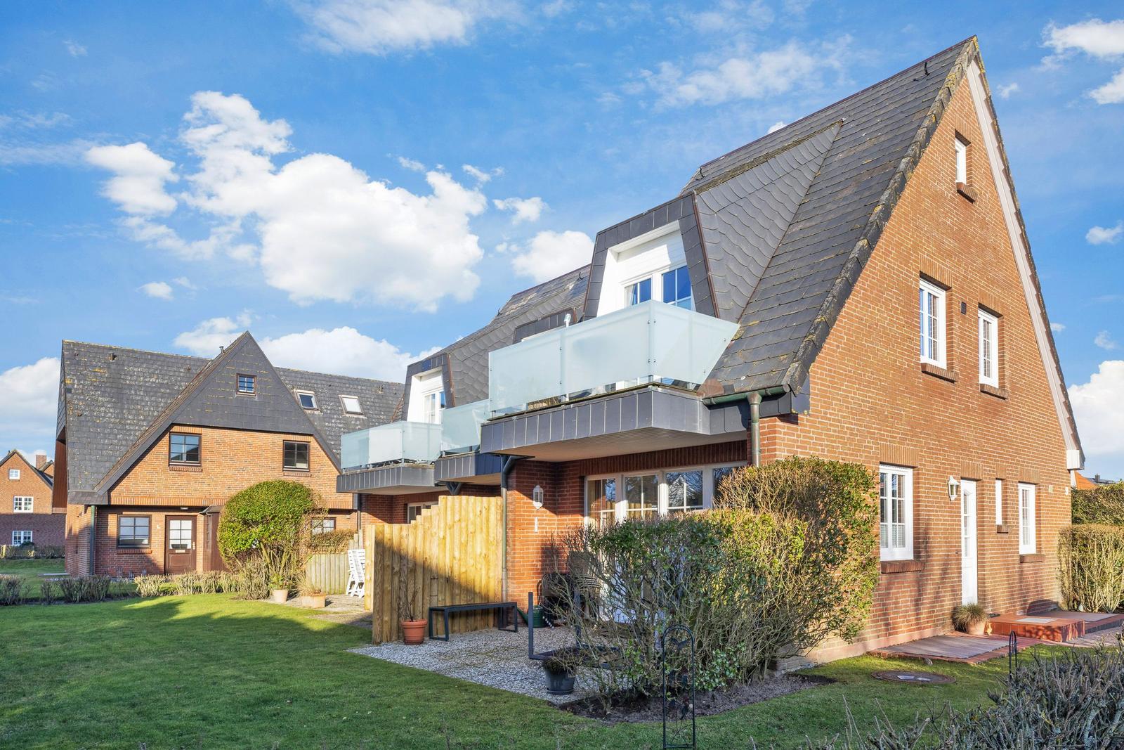 Red brick building with balcony and garden under blue sky.