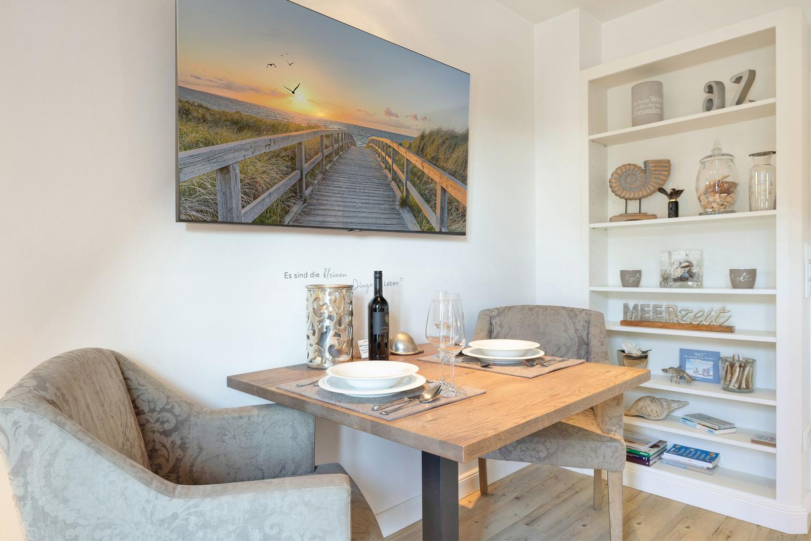 Dining table with two chairs, wall picture, and shelf with decorative items.