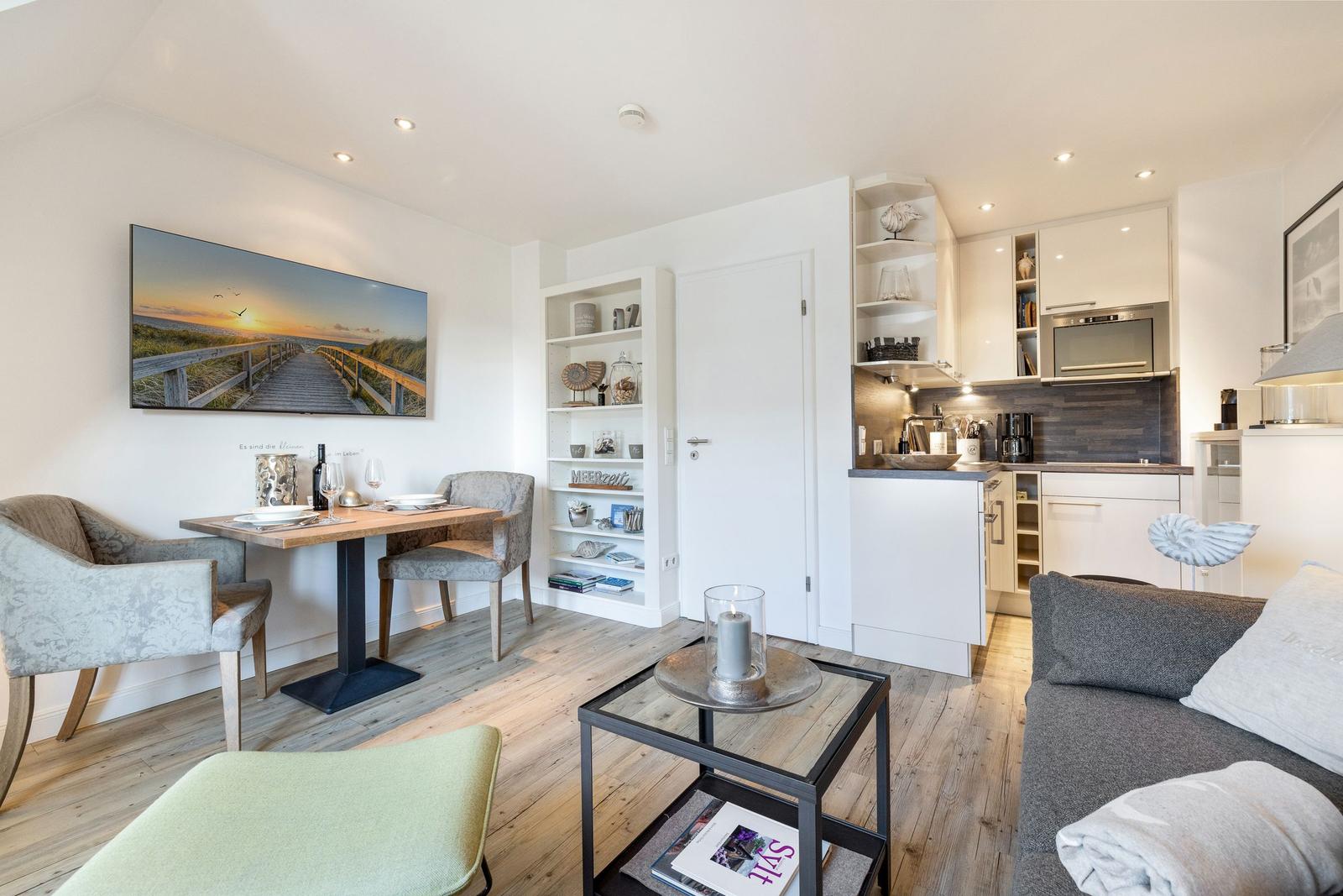 Living kitchen with dining table, sofa, and kitchen cabinets. Wooden floor and wall picture.