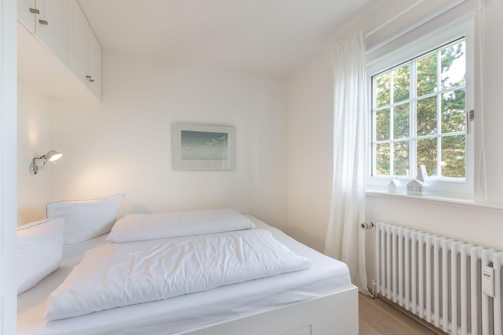 Schlafzimmer mit weißem Bett, Fenster und Heizkörper.
