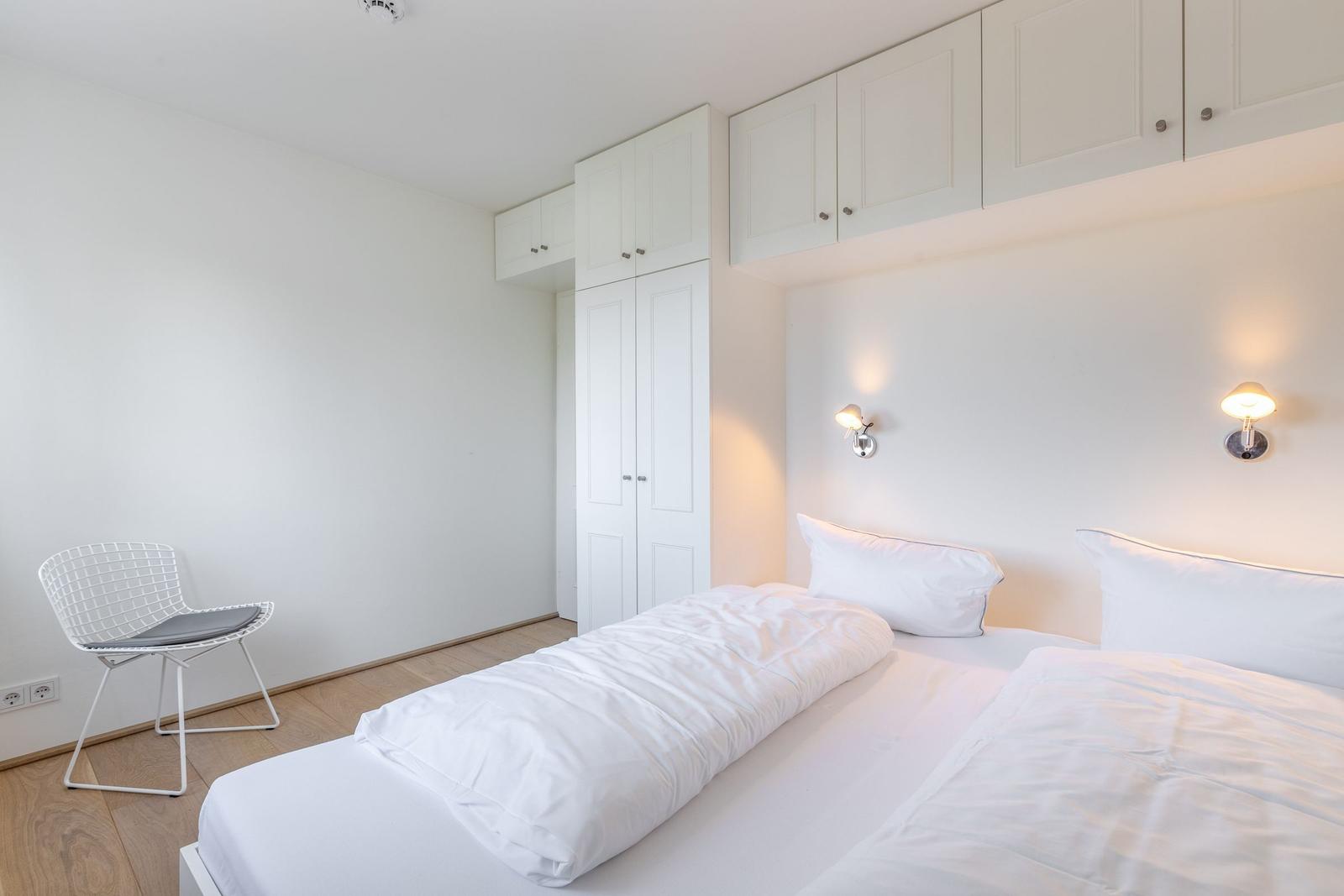 Schlafzimmer mit weißem Bett, Schrank und Stuhl.