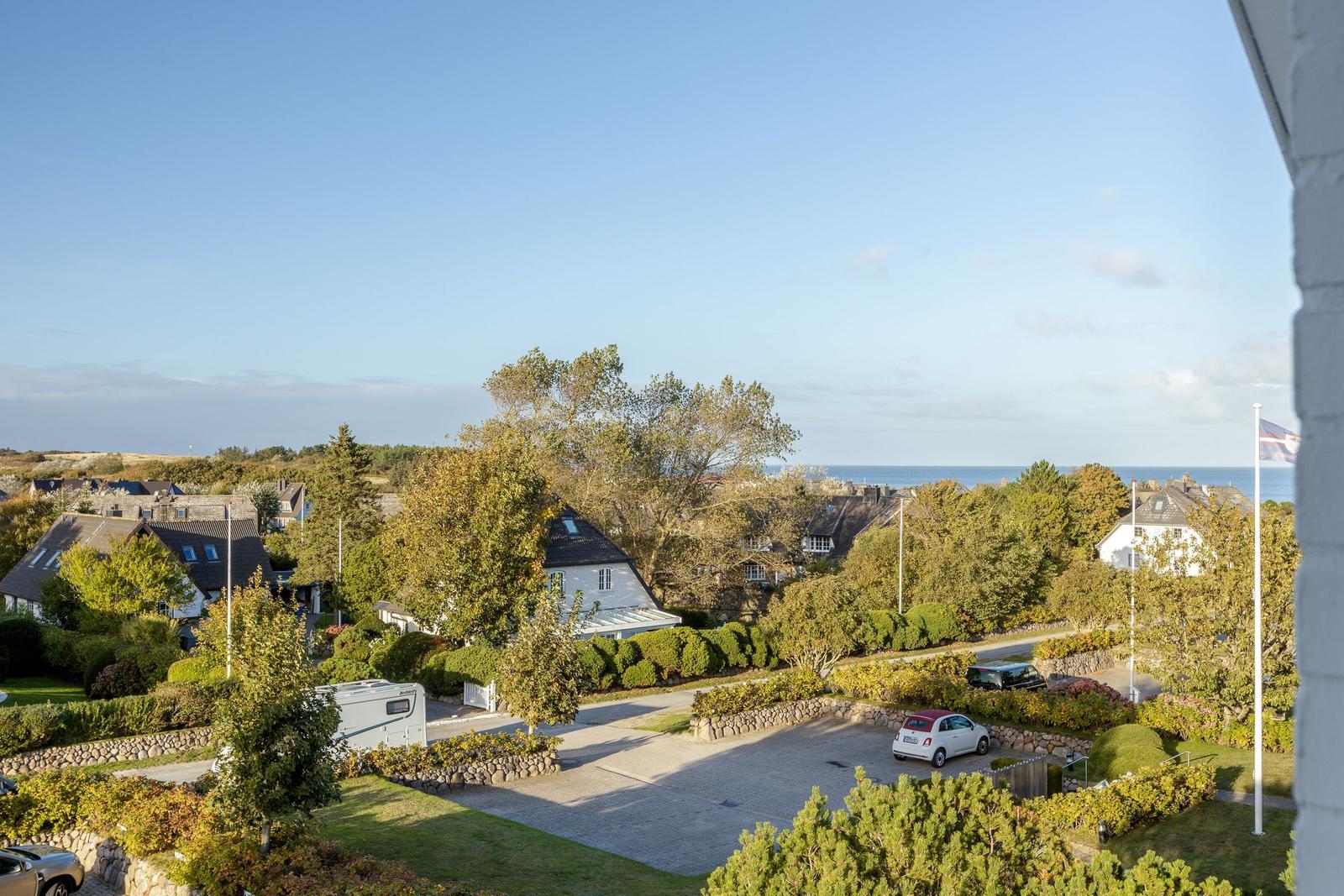 Weitläufiger Blick auf Wohnhäuser, Bäume und Meer unter blauem Himmel.