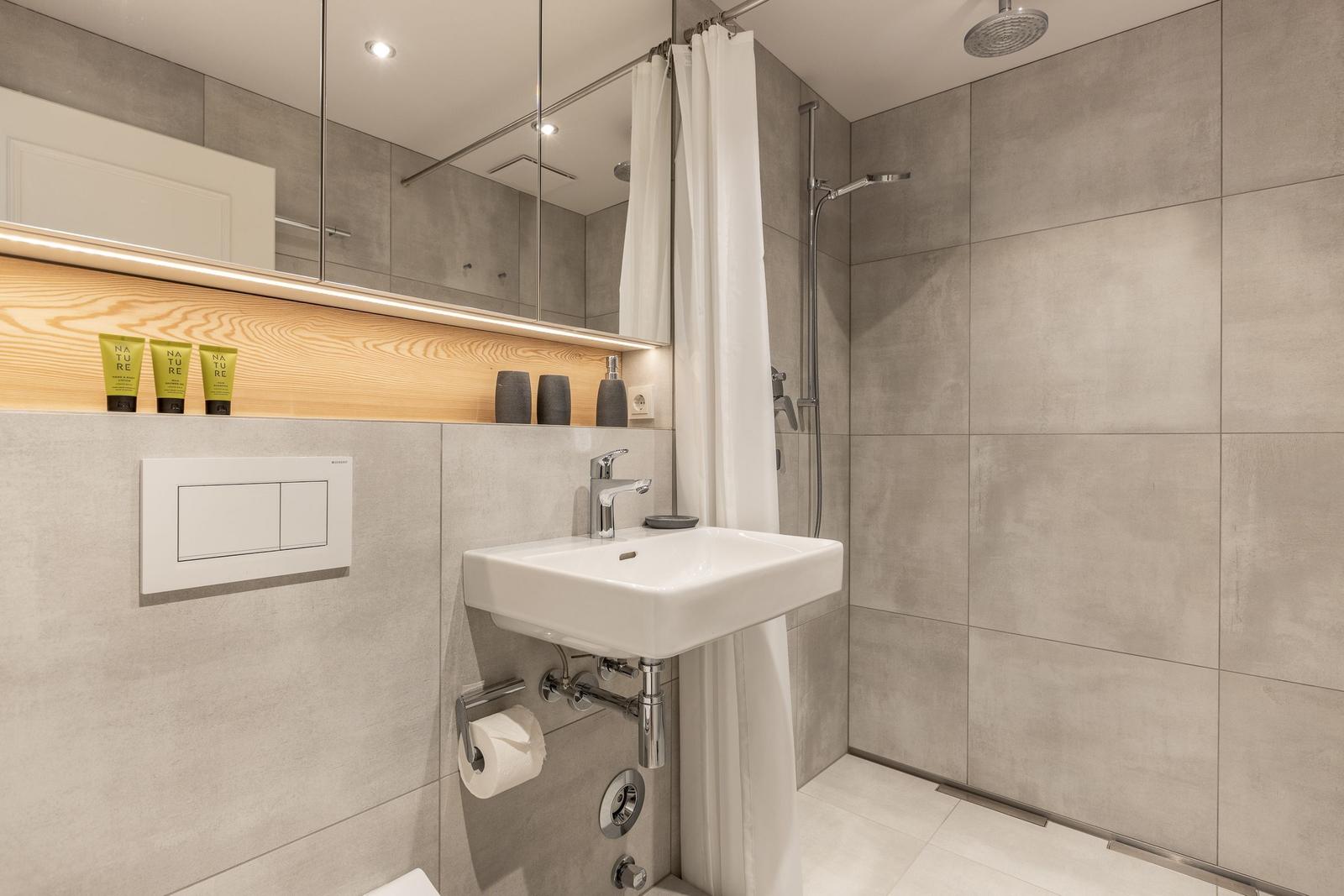 Bad mit Dusche, Waschbecken und Spiegelschrank. Holzregal mit Pflegeprodukten.