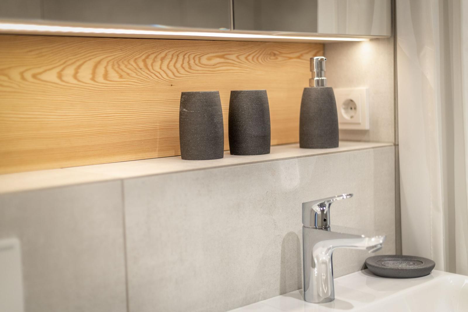 Waschbecken mit modernem Wasserhahn und grauen Accessoires auf Holz- und Steinuntergrund.