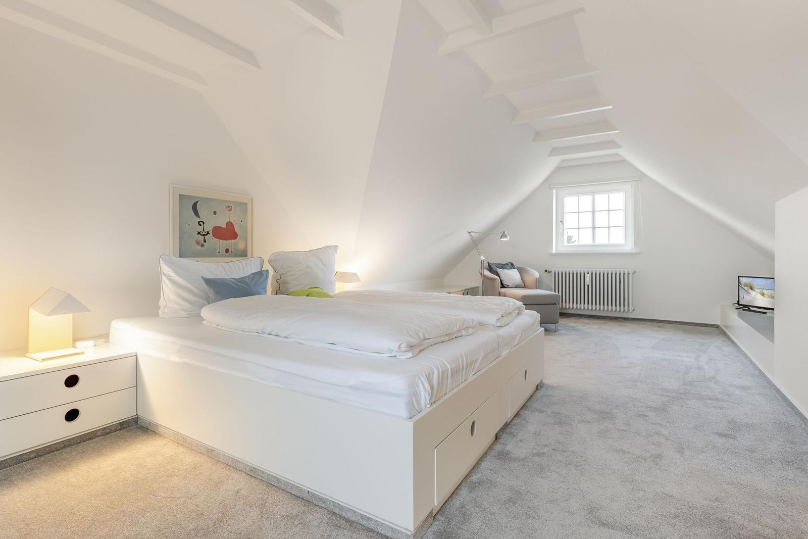 Schlafzimmer mit Dachschrägen, Bett, Nachttisch und Fernseher