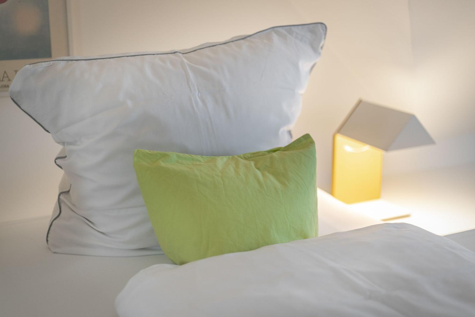 Bettkopf mit weißen und grünen Kissen, daneben eine Lampe.