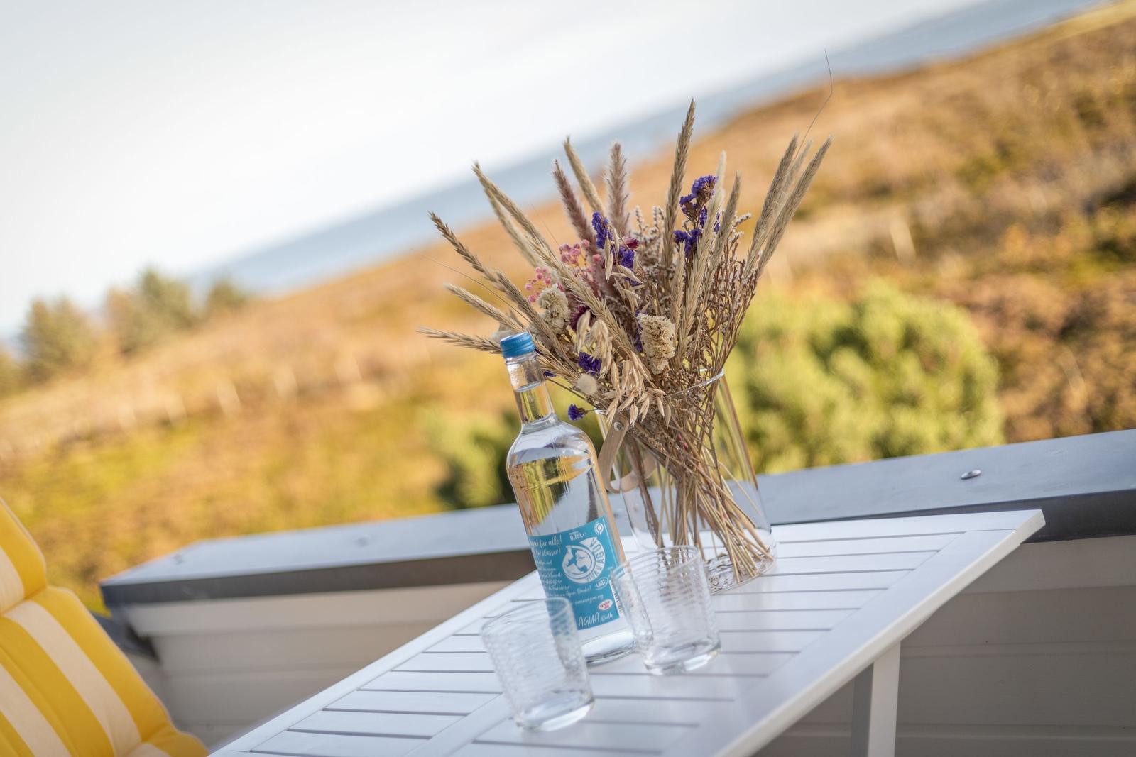Auf der Terrasse steht ein Tisch mit einer Flasche, Gläsern und einem Vasenarrangement.
