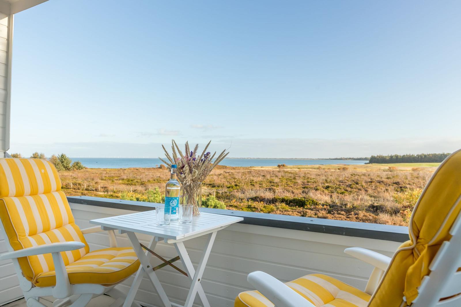 Terrasse mit zwei gelben Stühlen und Tisch. Blick auf Wasser und Feld.