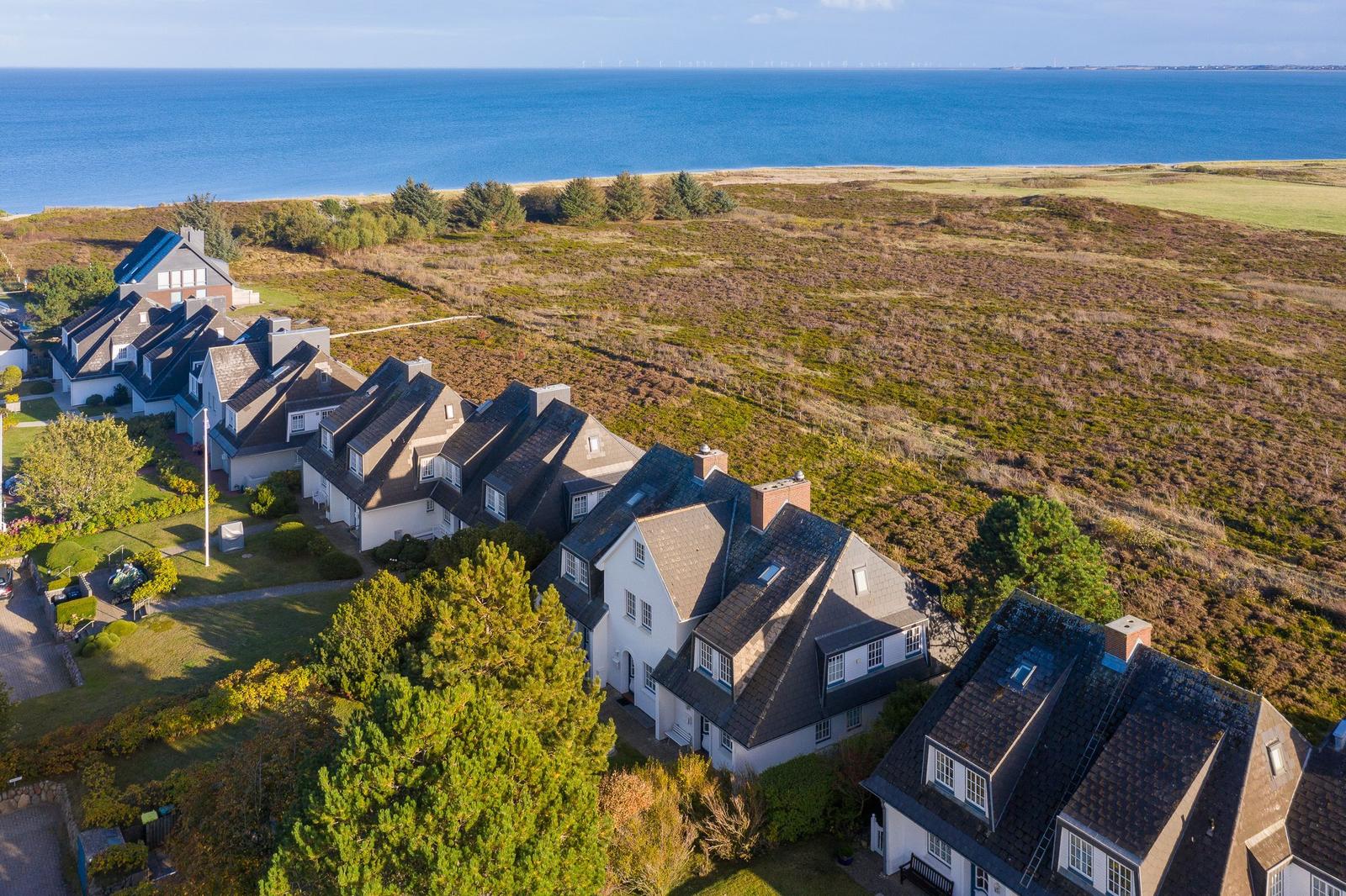 Häuser am Meer mit Grünflächen und Wiese im Hintergrund.