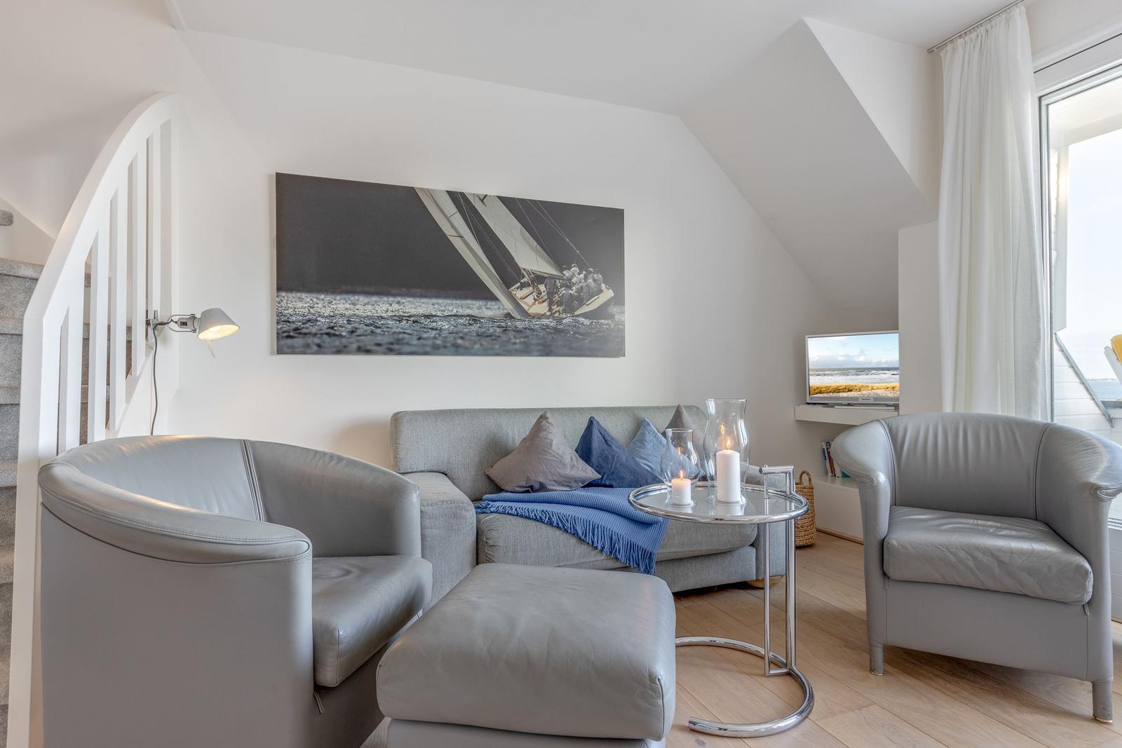 Wohnzimmer mit Sofa, zwei Sesseln und Wandbild. Holzboden und großes Fenster.