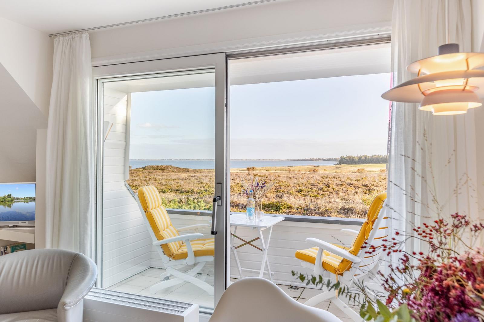Terrasse mit zwei gelben Sesseln und Tisch. Blick auf Wasser und Grasland.