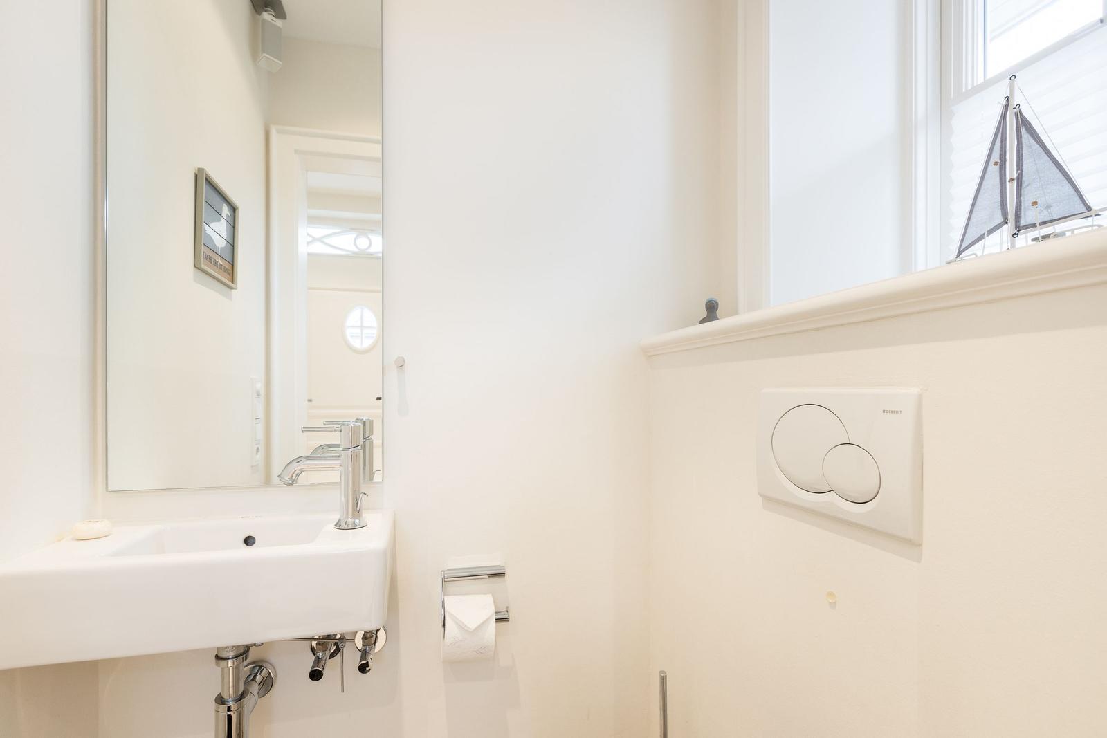 Badezimmer mit Waschbecken, Spiegel und Fenster mit Segelbootmodell.