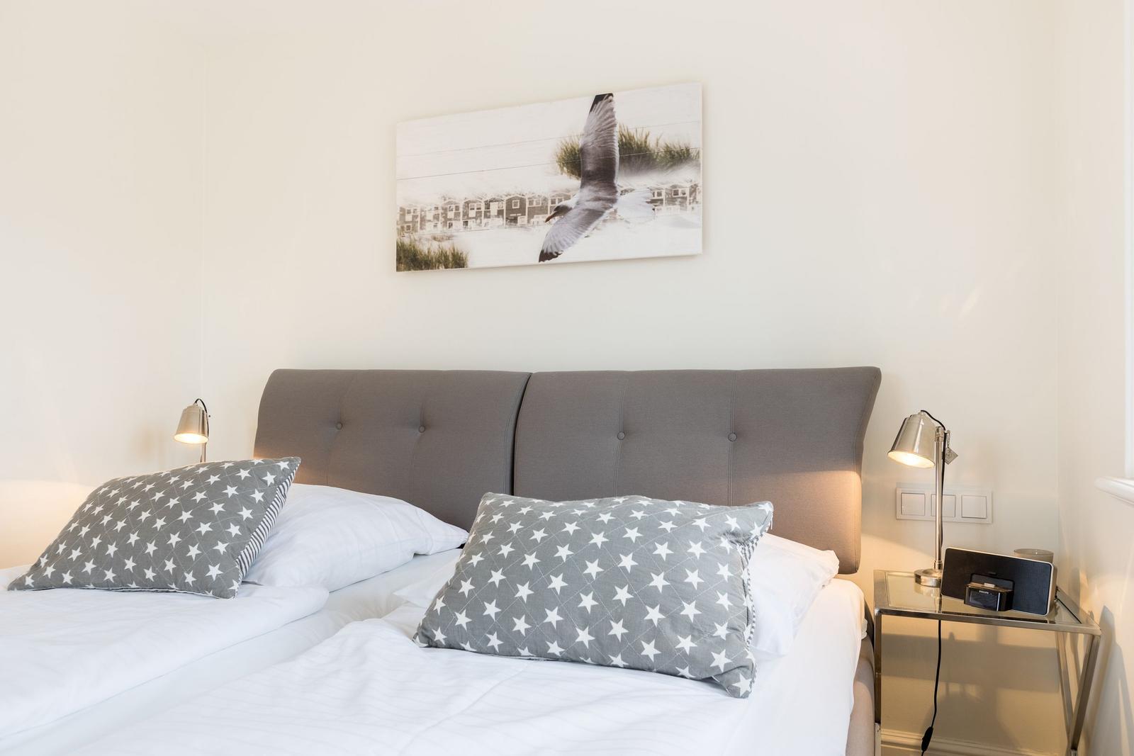 Schlafzimmer mit Bett, Kopfkissen und Wandbild.