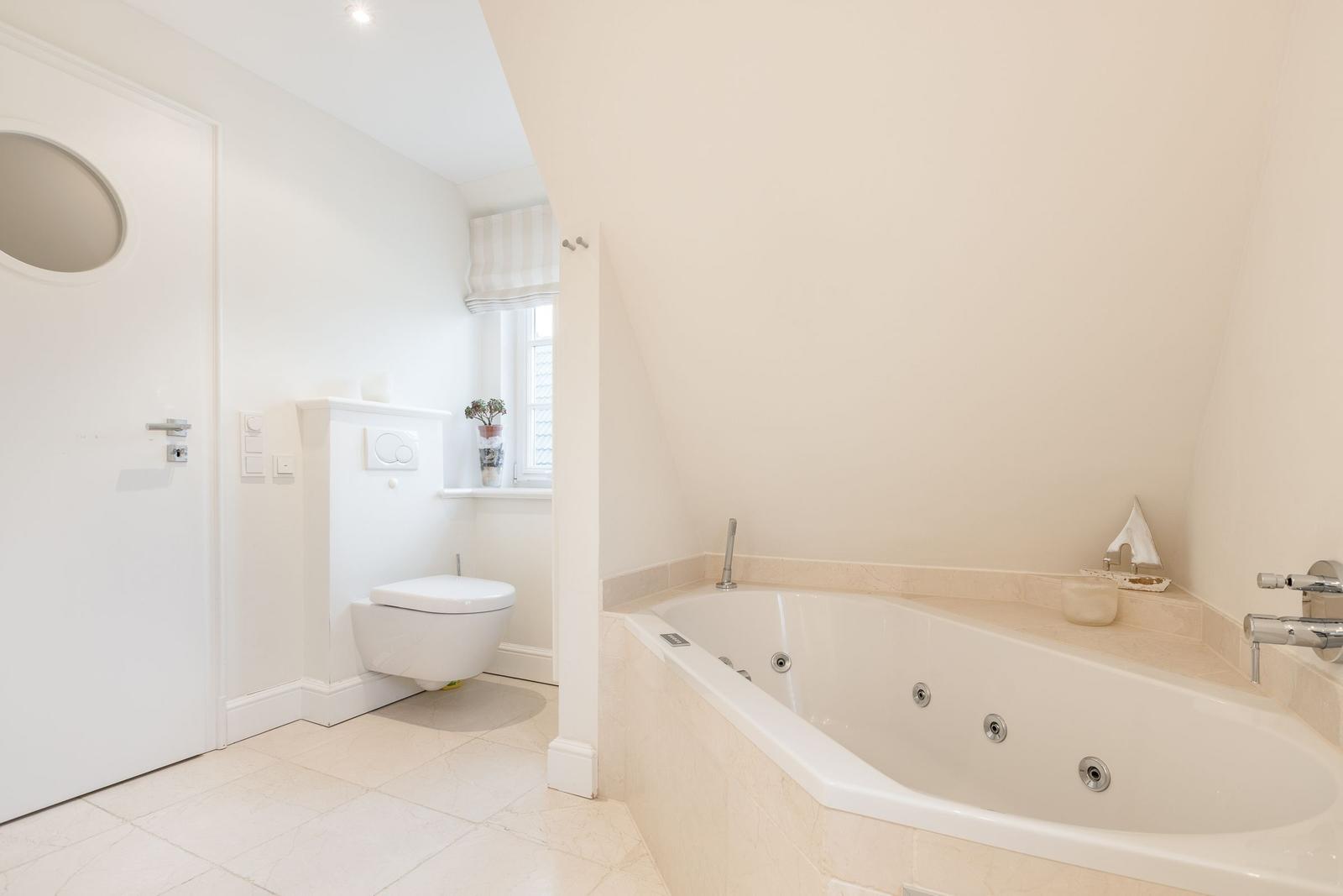 Bad mit Whirlpool, Toilette und Fenster mit Rollladen.