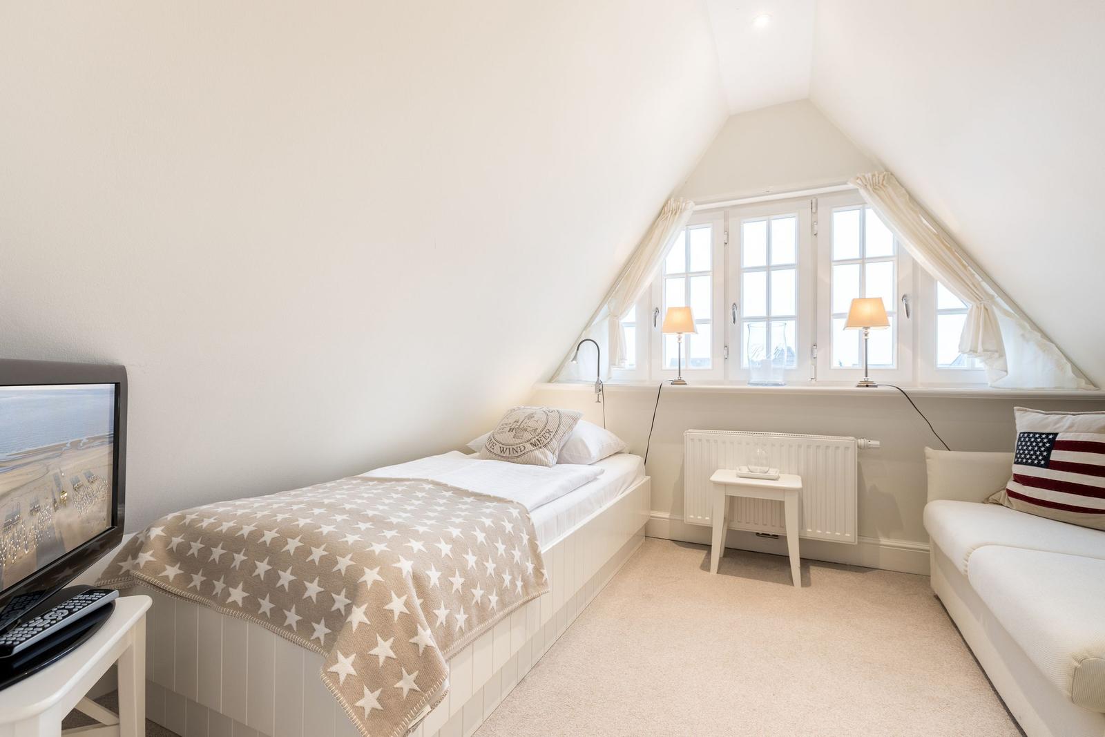 Schlafzimmer mit Einzelbett, Sofa und Fenster mit Vorhängen.