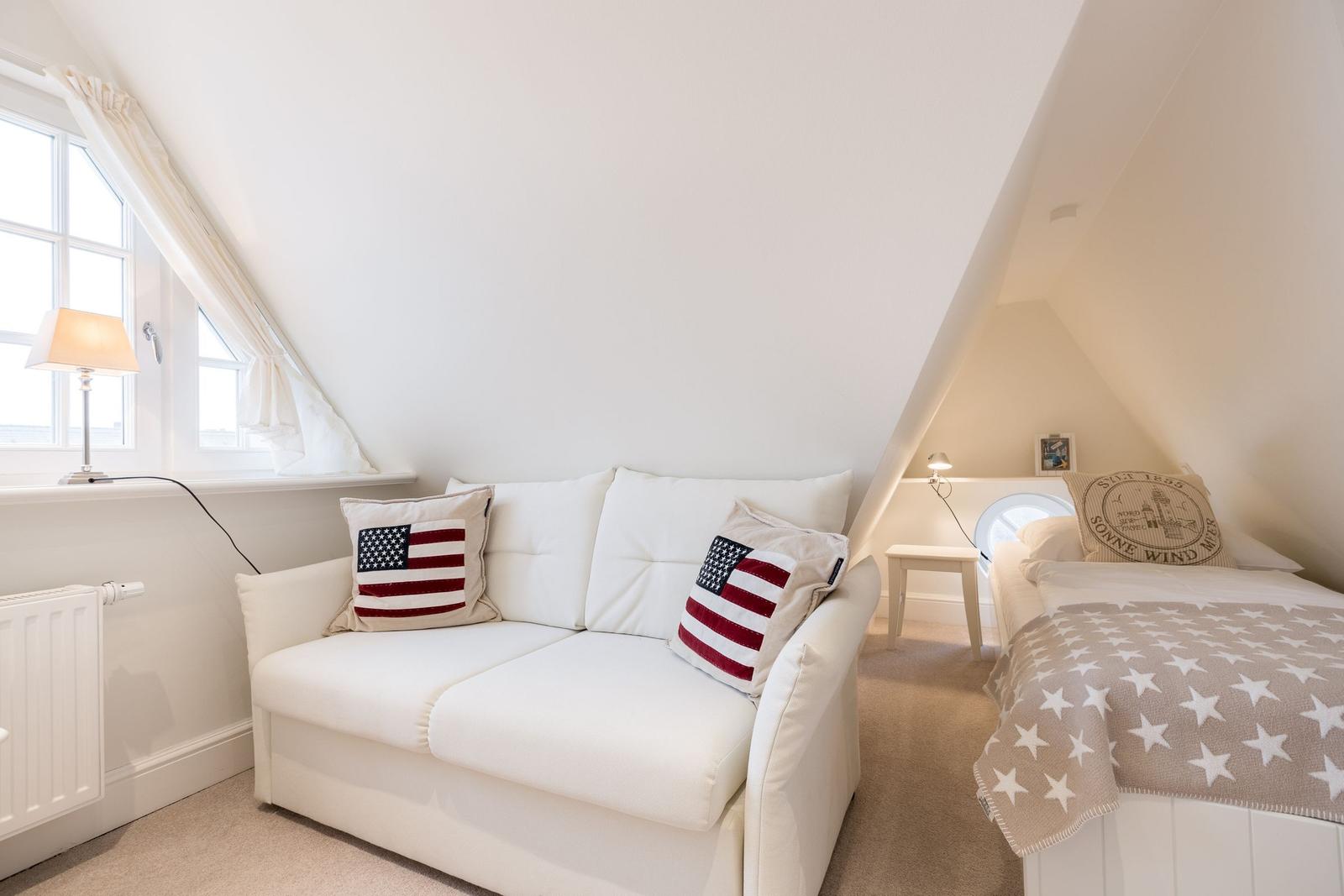 Schlafzimmer mit Sofa, Bett und Fenster unter Dachschrägen.