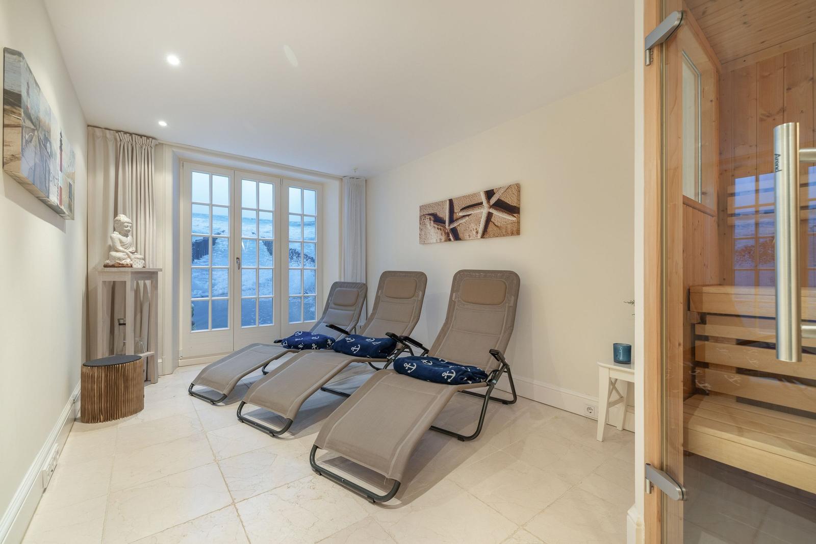 Drei Liegestühle vor Fenster mit Meerblick. Sauna im Hintergrund.