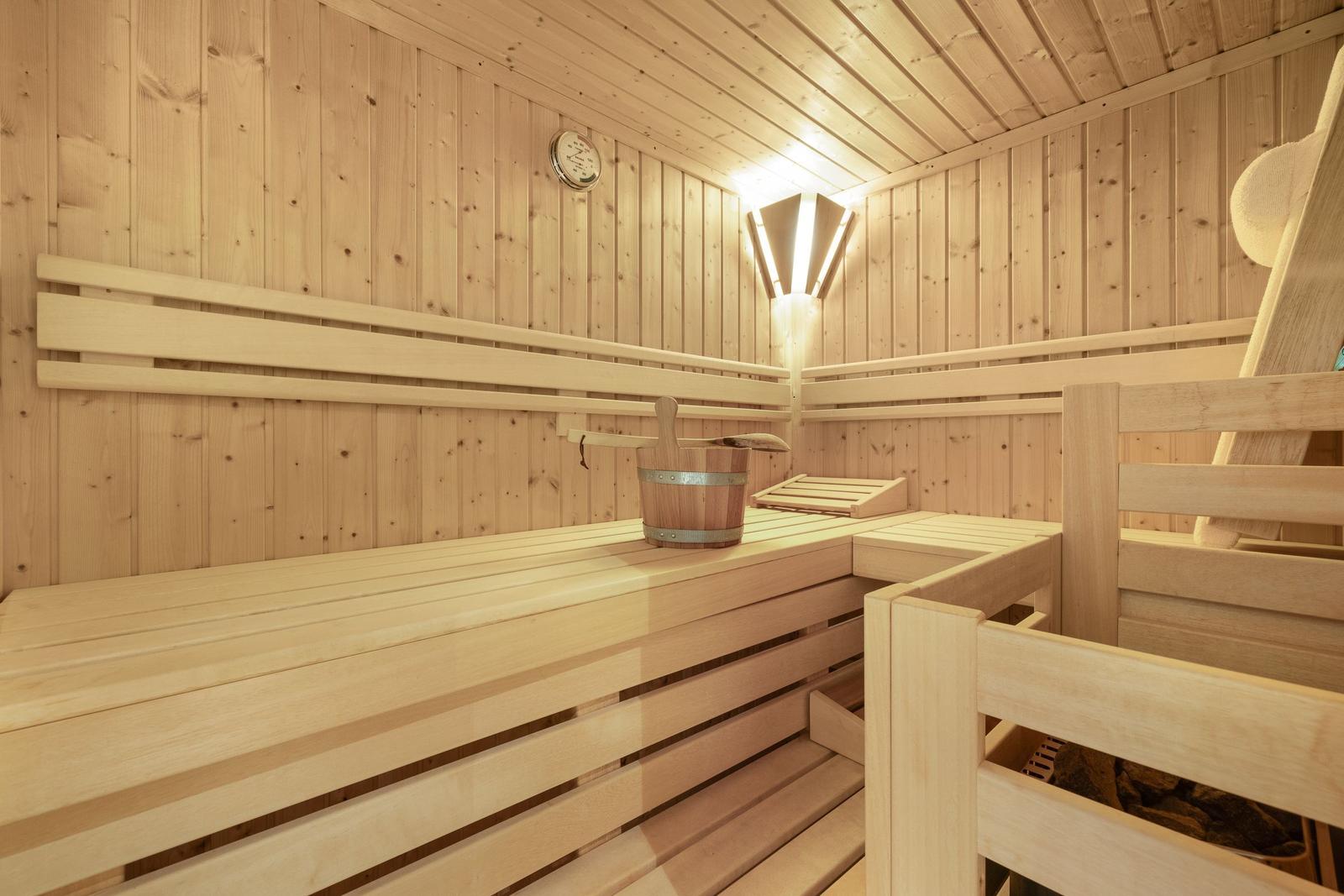 Holzsauna mit Bank, Eimer und Thermometer an der Wand.
