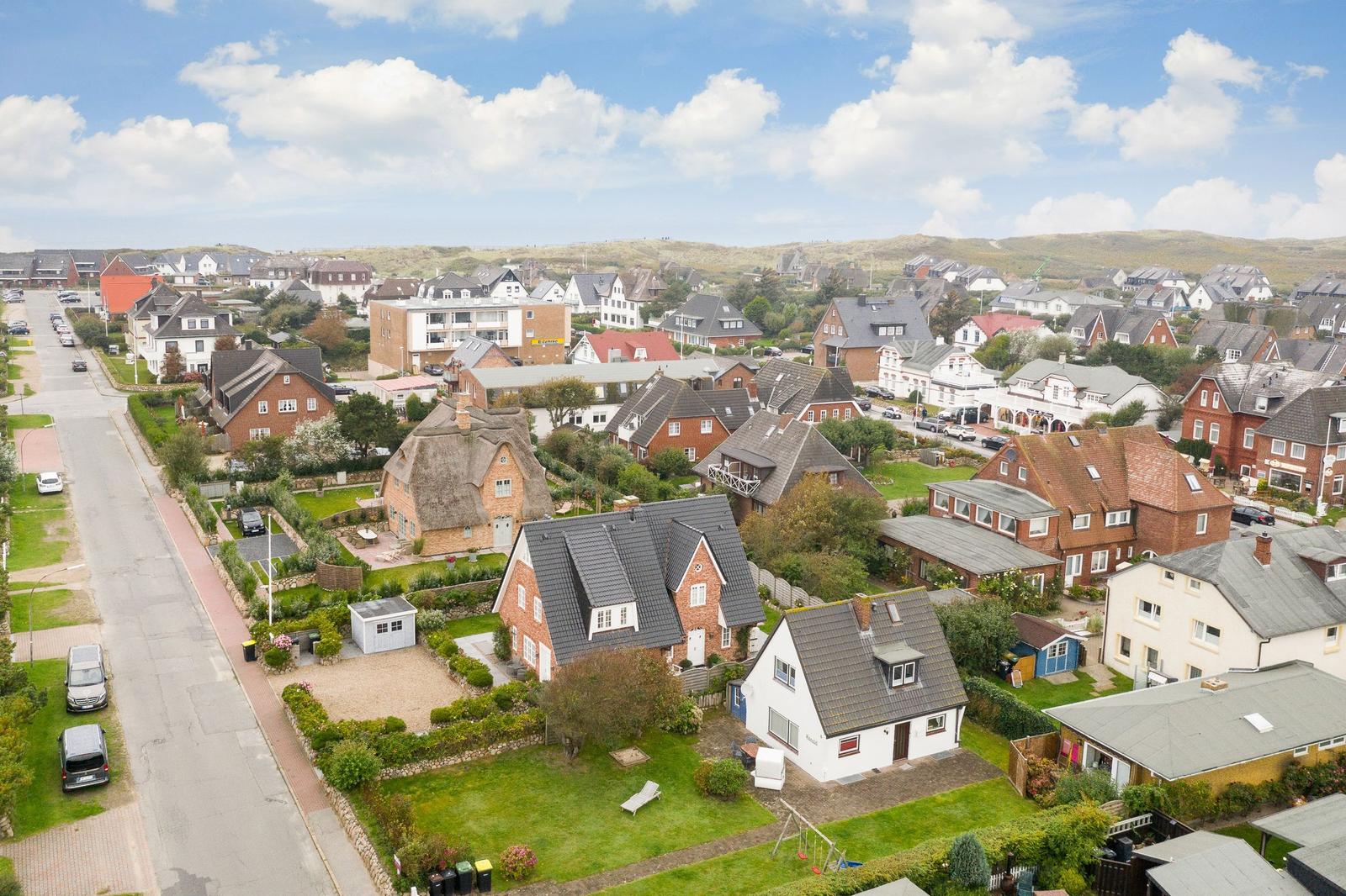 Dorf mit Häusern, Gärten und Straßen unter blauem Himmel.