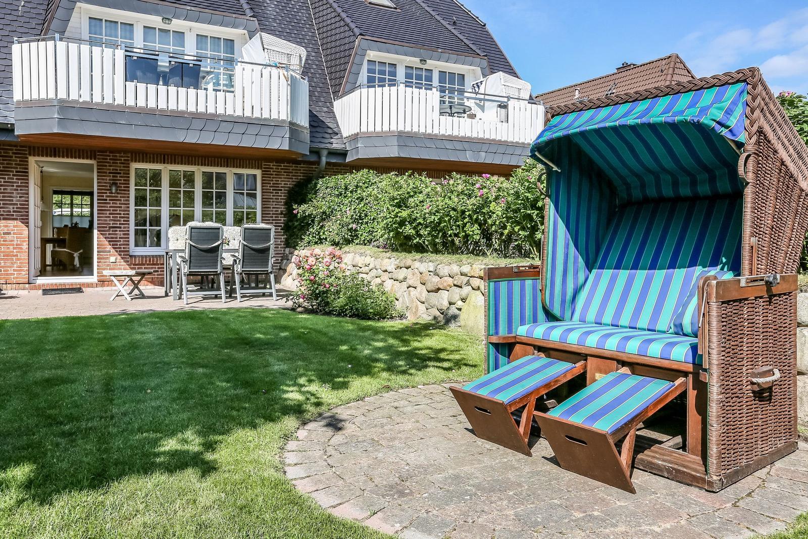Hinterhof mit Strandkorb, Grasfläche und Terrasse vor einem Haus.