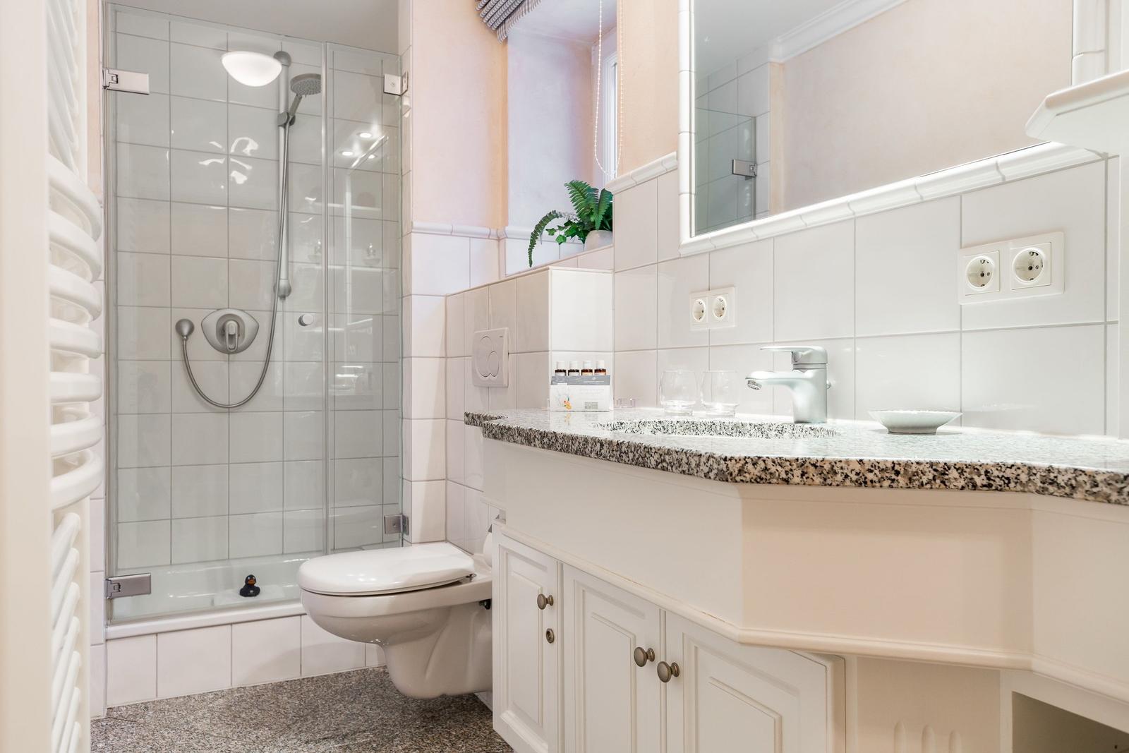 Bad mit Dusche, Waschbecken und Toilette. Weiße Fliesen und Marmorarbeitsplatte.