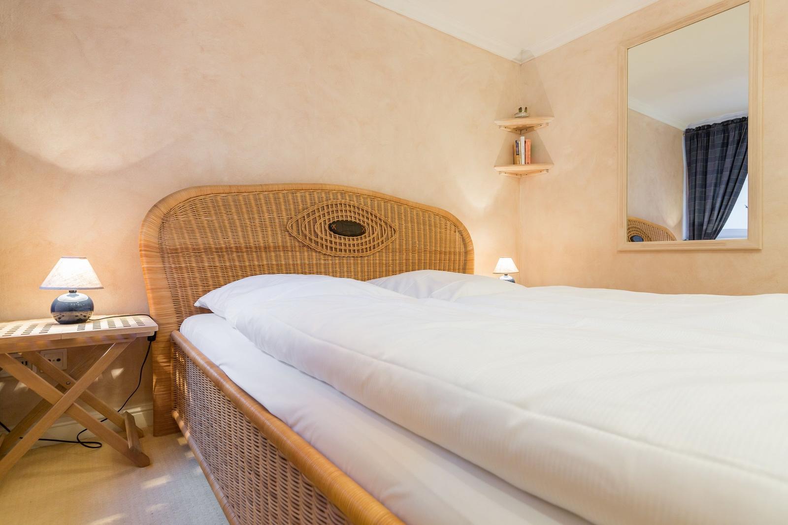 Schlafzimmer mit Rattanbett, Nachttisch und Spiegel an der Wand.