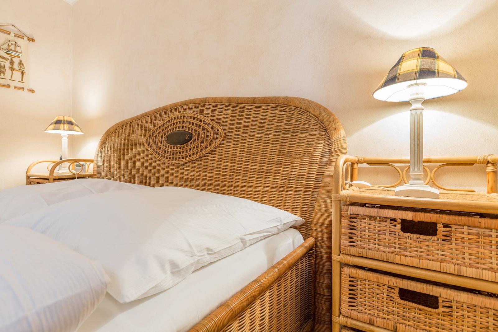 Schlafzimmer mit Rattanbett und Nachttisch mit Lampe.