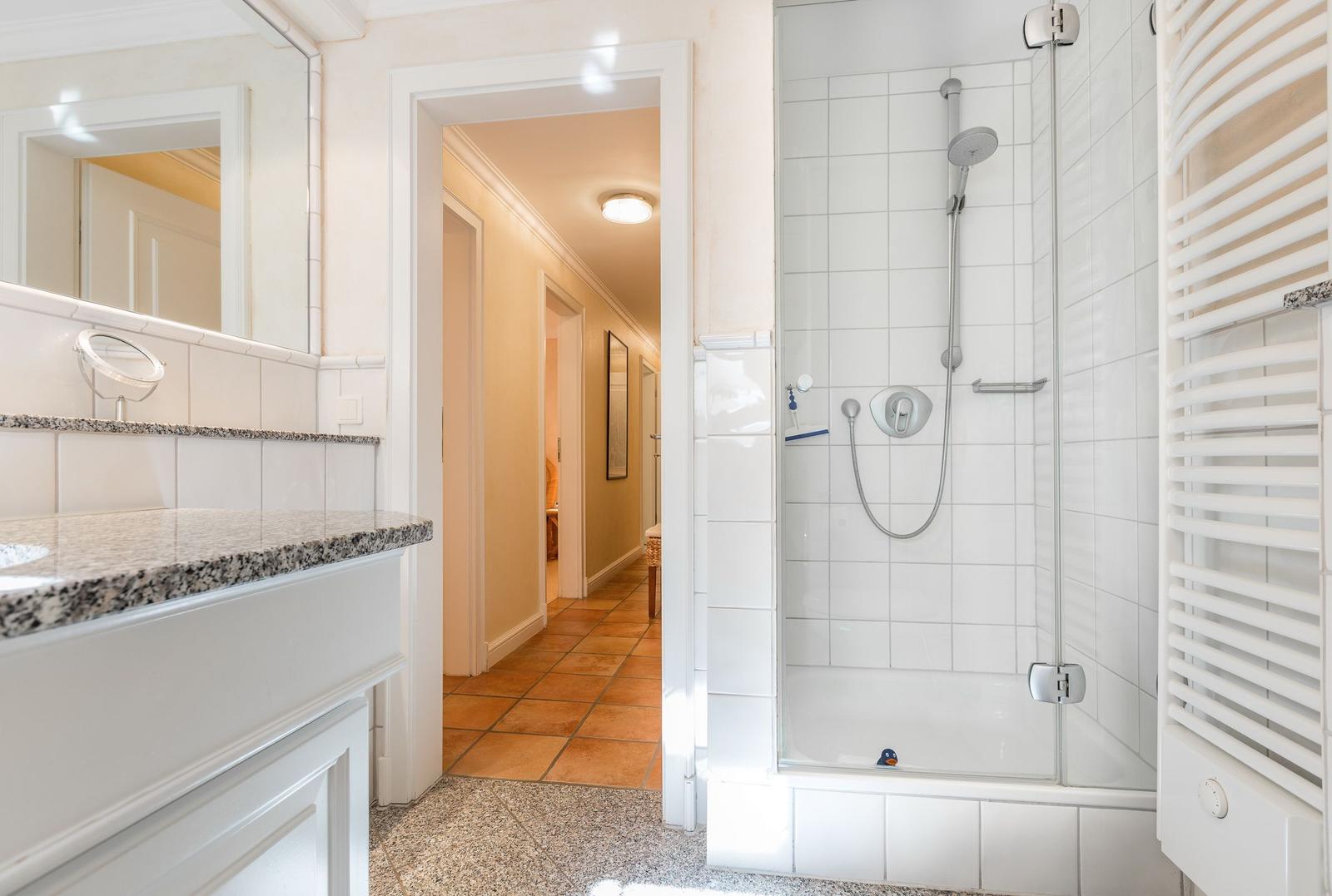 Badezimmer mit Dusche, Waschtisch und Heizung.