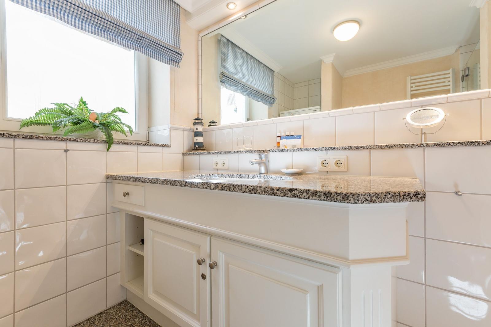 Badezimmer mit Waschbecken, Spiegel und Fenster mit Pflanze.
