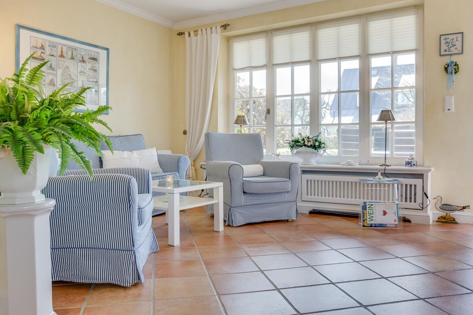 Wohnzimmer mit blau-weißen Sesseln, Glas-Tisch und Fenster mit Jalousien.