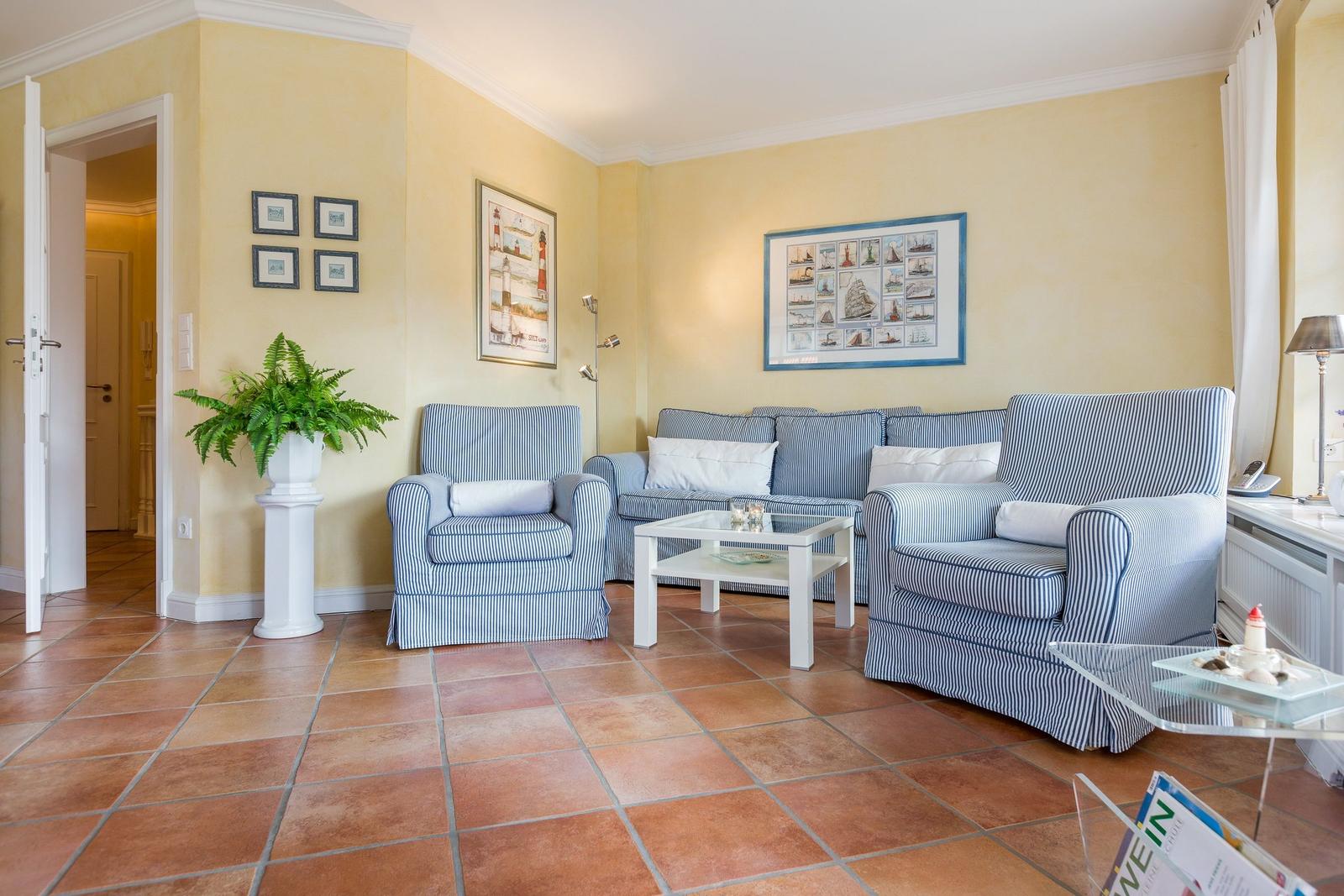 Wohnzimmer mit blau-weißen Sesseln, Couch und Glas-Tisch auf Terrakottboden.