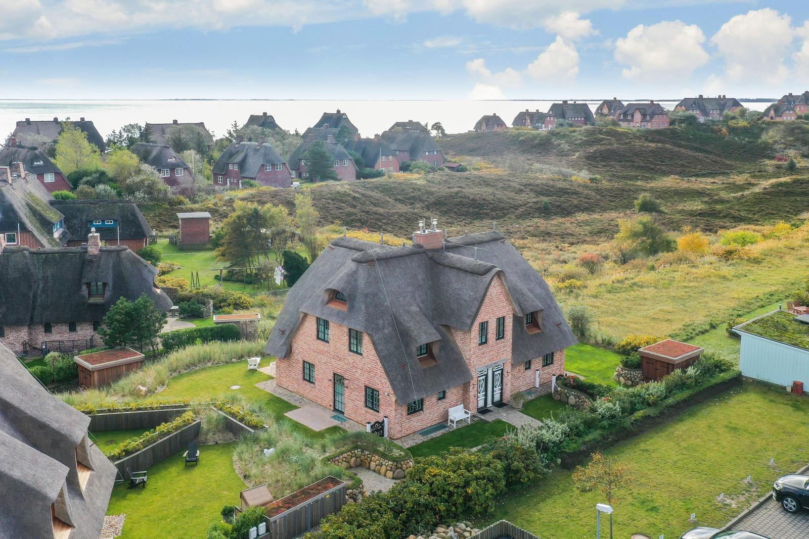 Haus mit Strohdach und Garten, Blick auf Strand und Hügel.