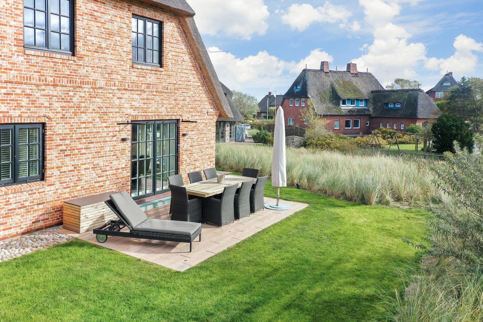 Roter Backsteinhaus mit Terrasse, Garten und Sitzgruppe. Hintergrund: Dächer mit Schilf.