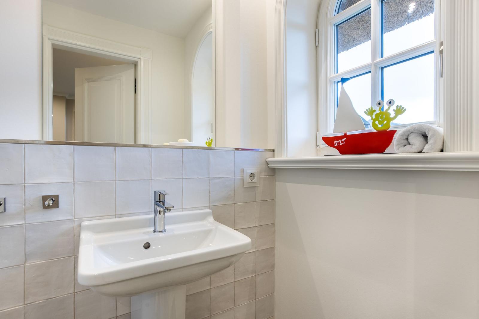 Badezimmer mit Waschbecken, Spiegel und Fenster mit Segelboot.