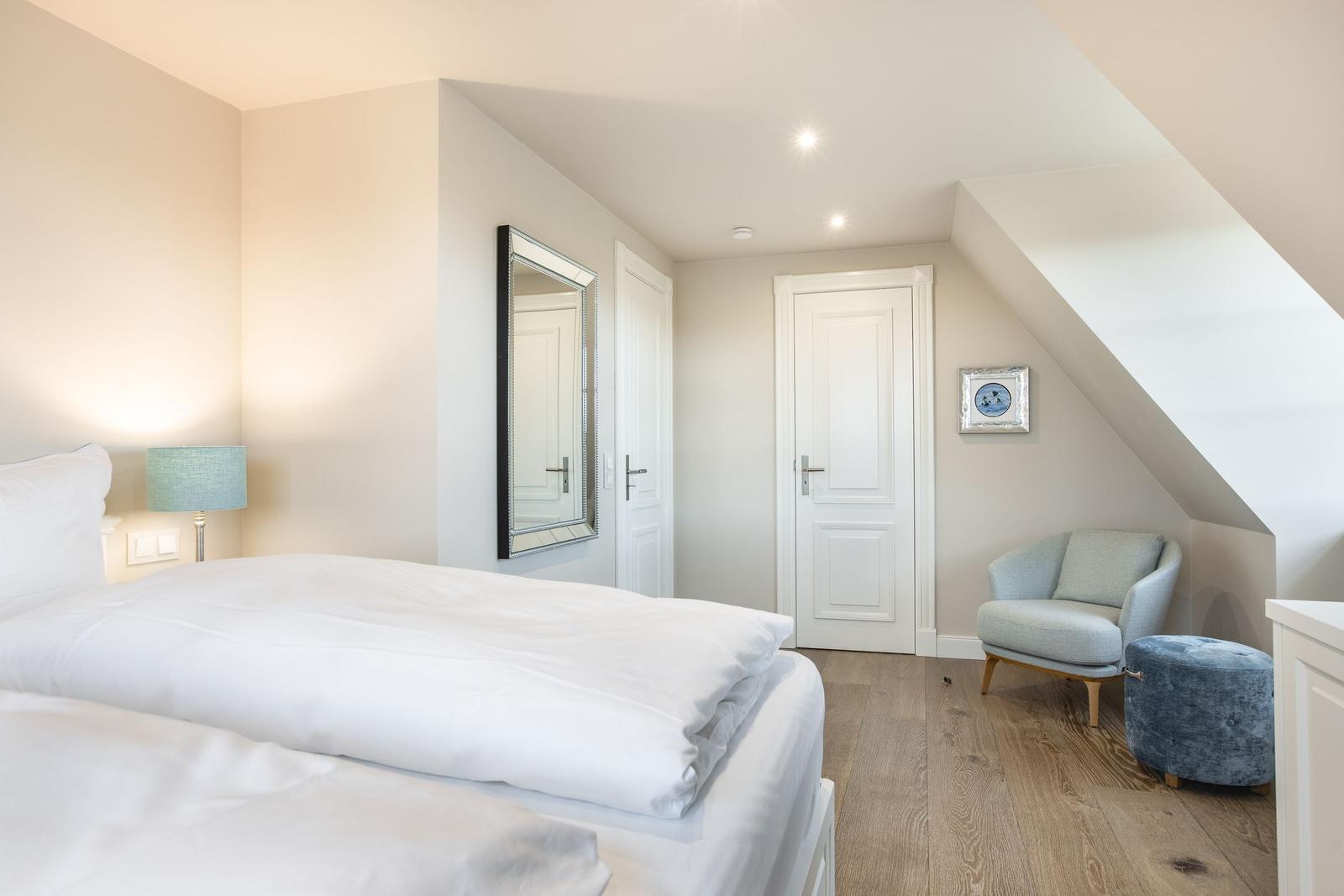 Schlafzimmer mit Dachschrägen, Bett, Sessel und Spiegel.