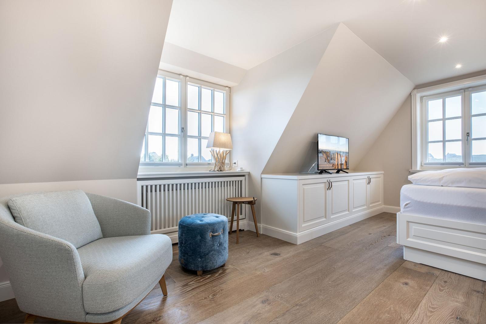 Schlafzimmer mit Dachschrägen, Fenstern, Bett, TV und Sessel.