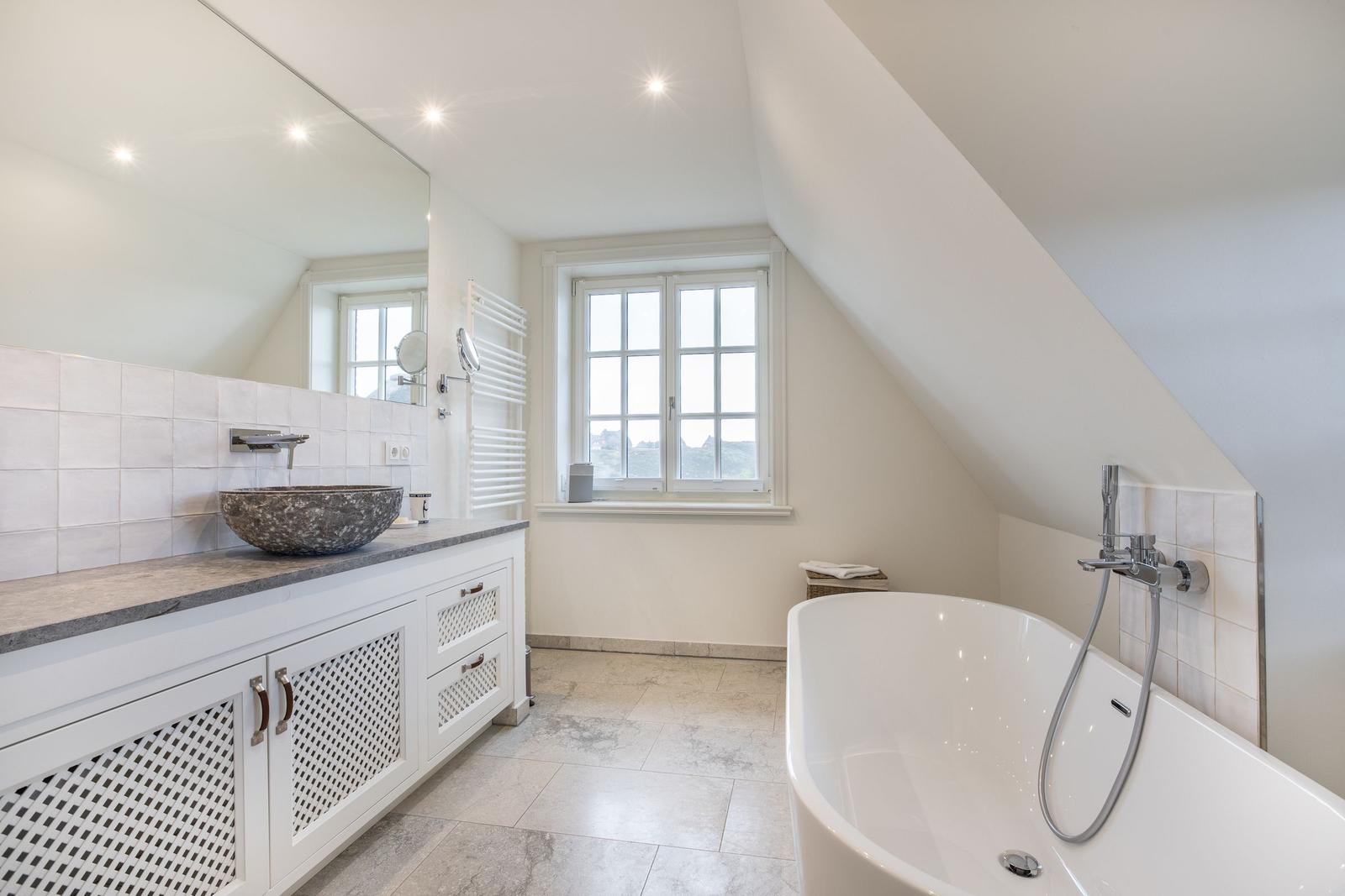 Badezimmer mit freistehender Badewanne, Waschtisch und Fenster
