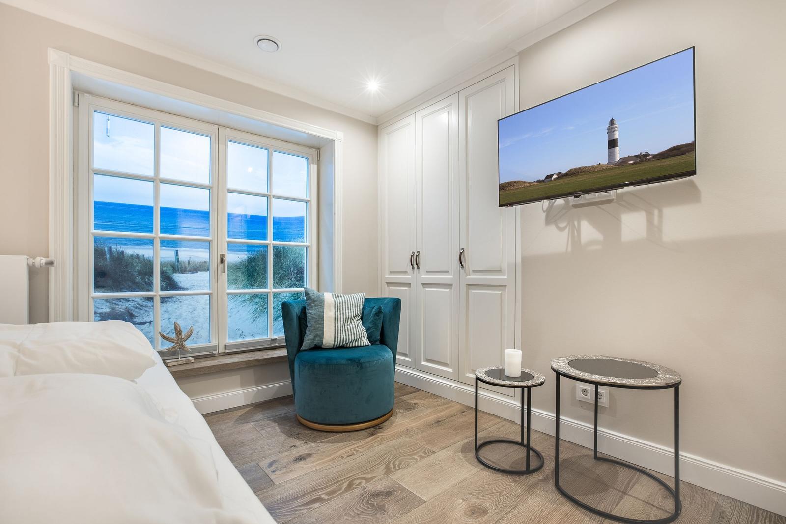 Zimmer mit Blick aufs Meer, blauer Sessel, TV und Kleiderschrank.
