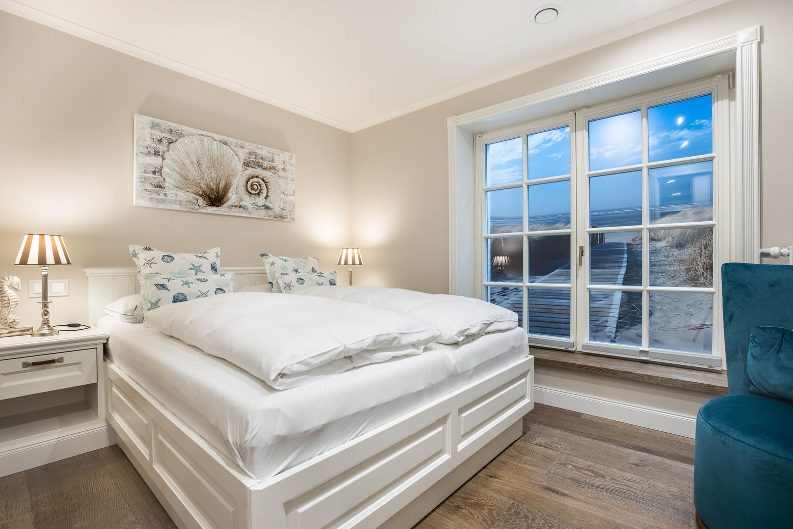 Schlafzimmer mit Blick auf Strand und Meer durch große Fenster.