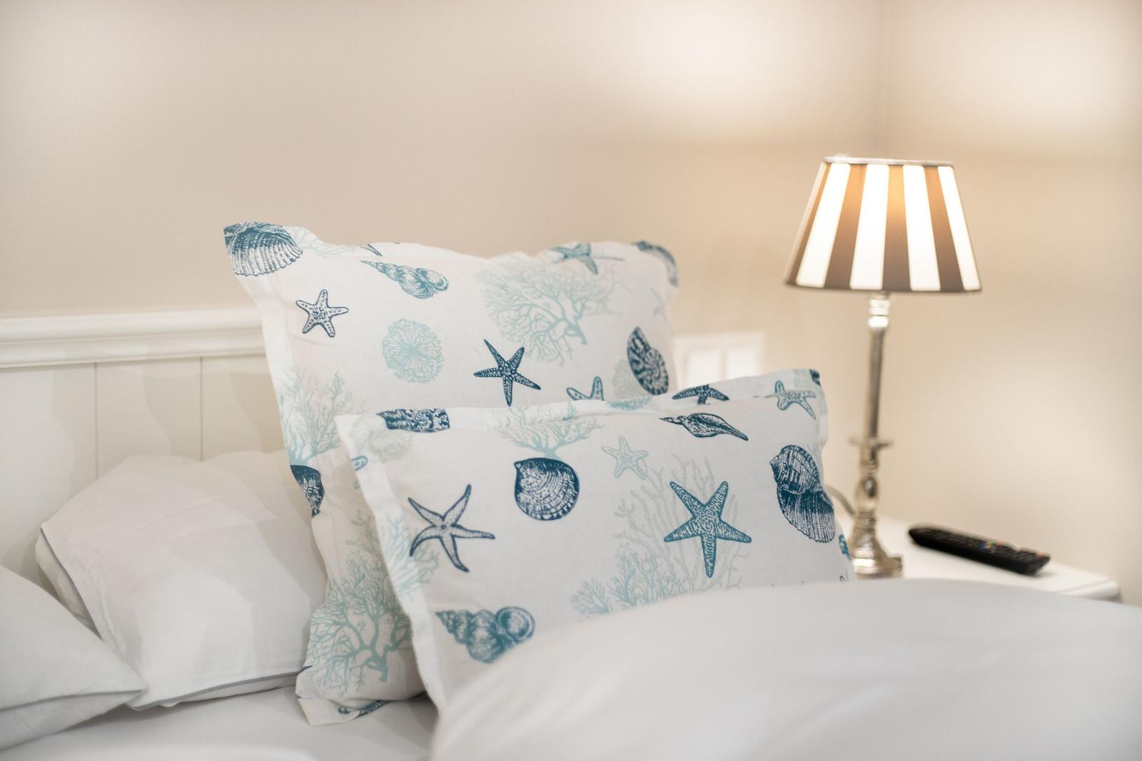 Bettkopf mit Kissen in Seestern-Muster, Nachttisch mit Lampe und Fernbedienung.
