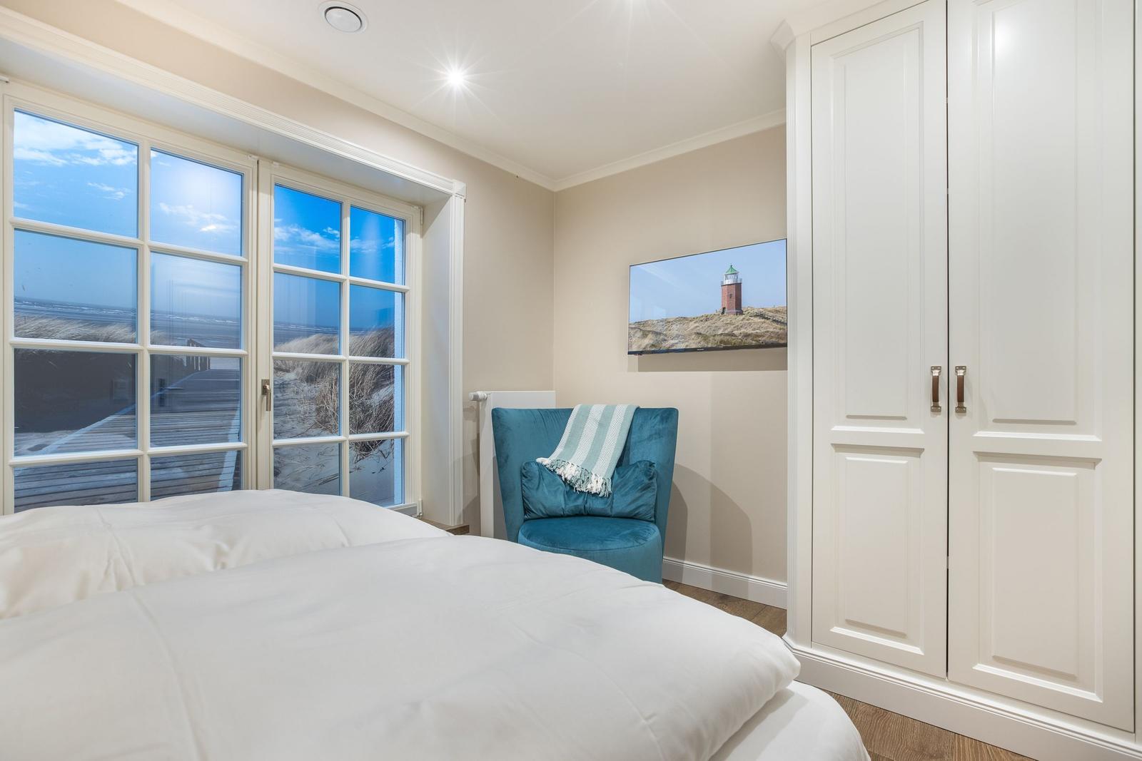 Schlafzimmer mit Blick auf Strand, blauer Sessel und weißer Kleiderschrank.
