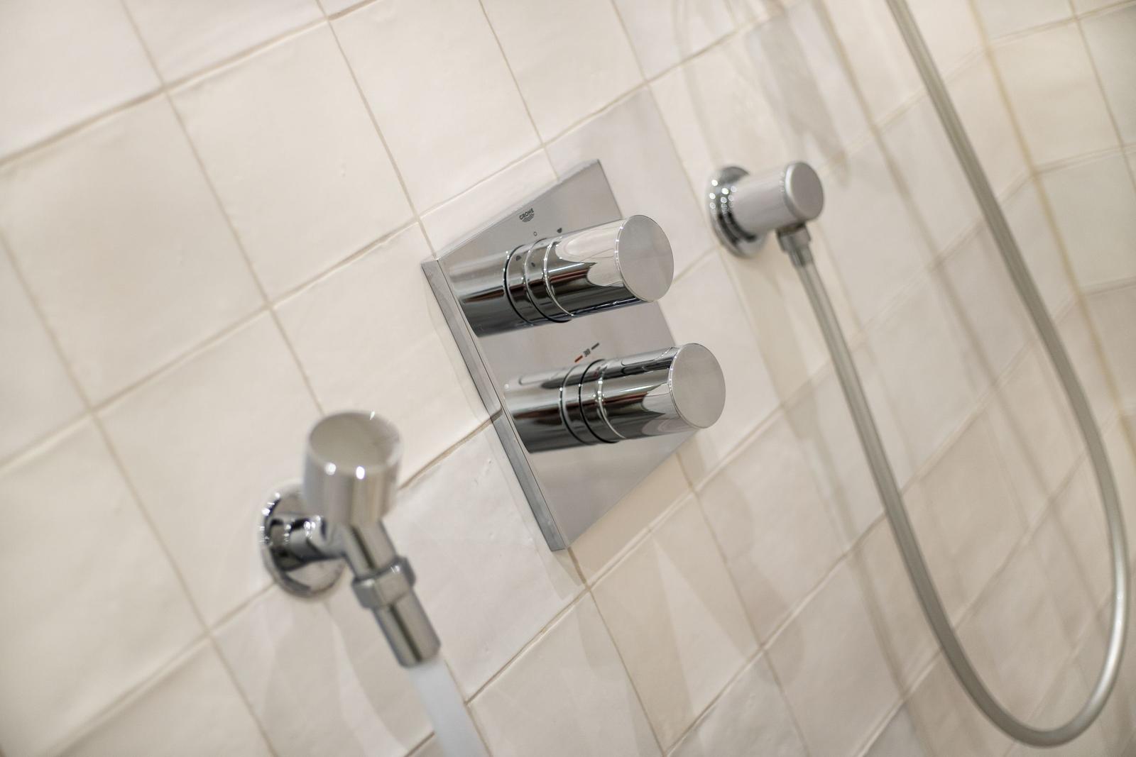 Duschkopf und Wasserhahn mit zwei Knöpfen an Wand