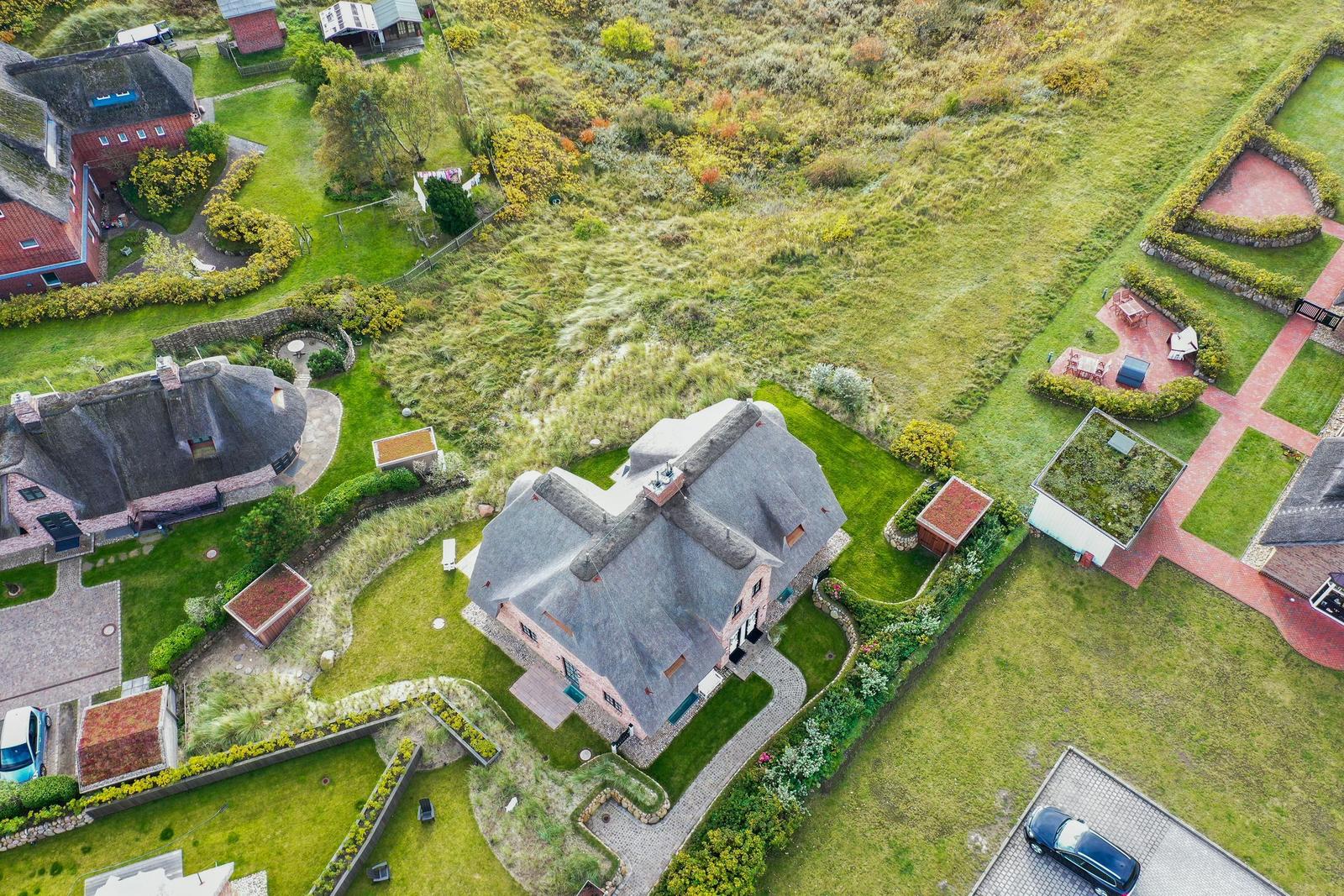 Dorfhaus mit Dach aus Stroh, umgeben von Grünflächen und gepflegten Gärten.