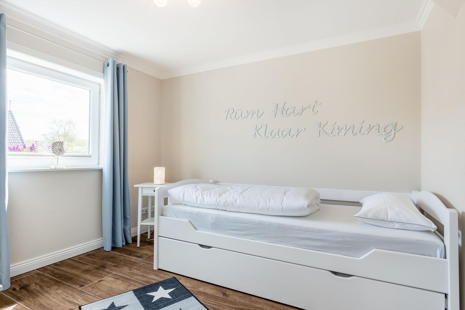 Schlafzimmer mit weißem Bett, Fenster und Wanddekoration.