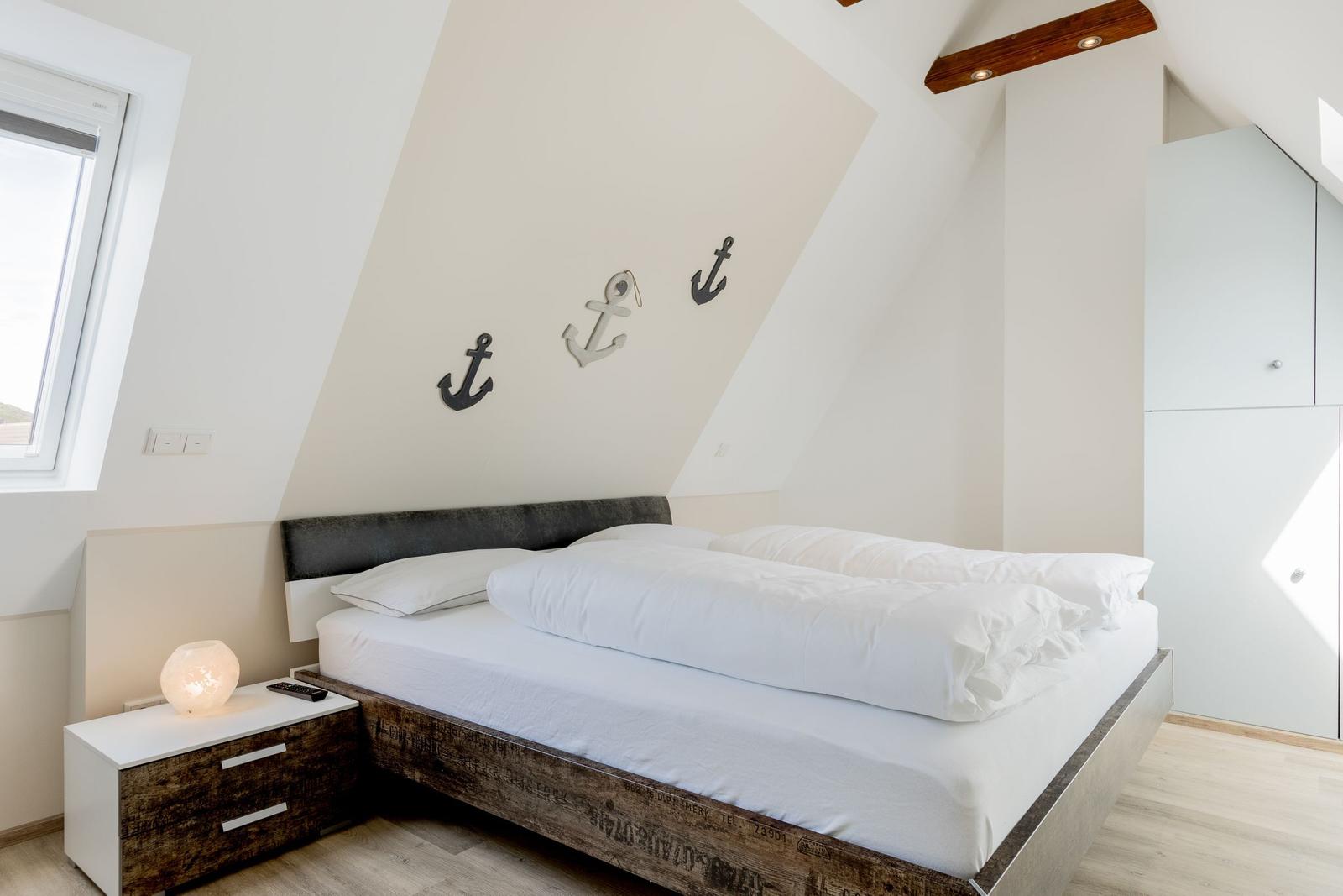 Schlafzimmer mit Doppelbett, Ankerdekoration und Fenster.